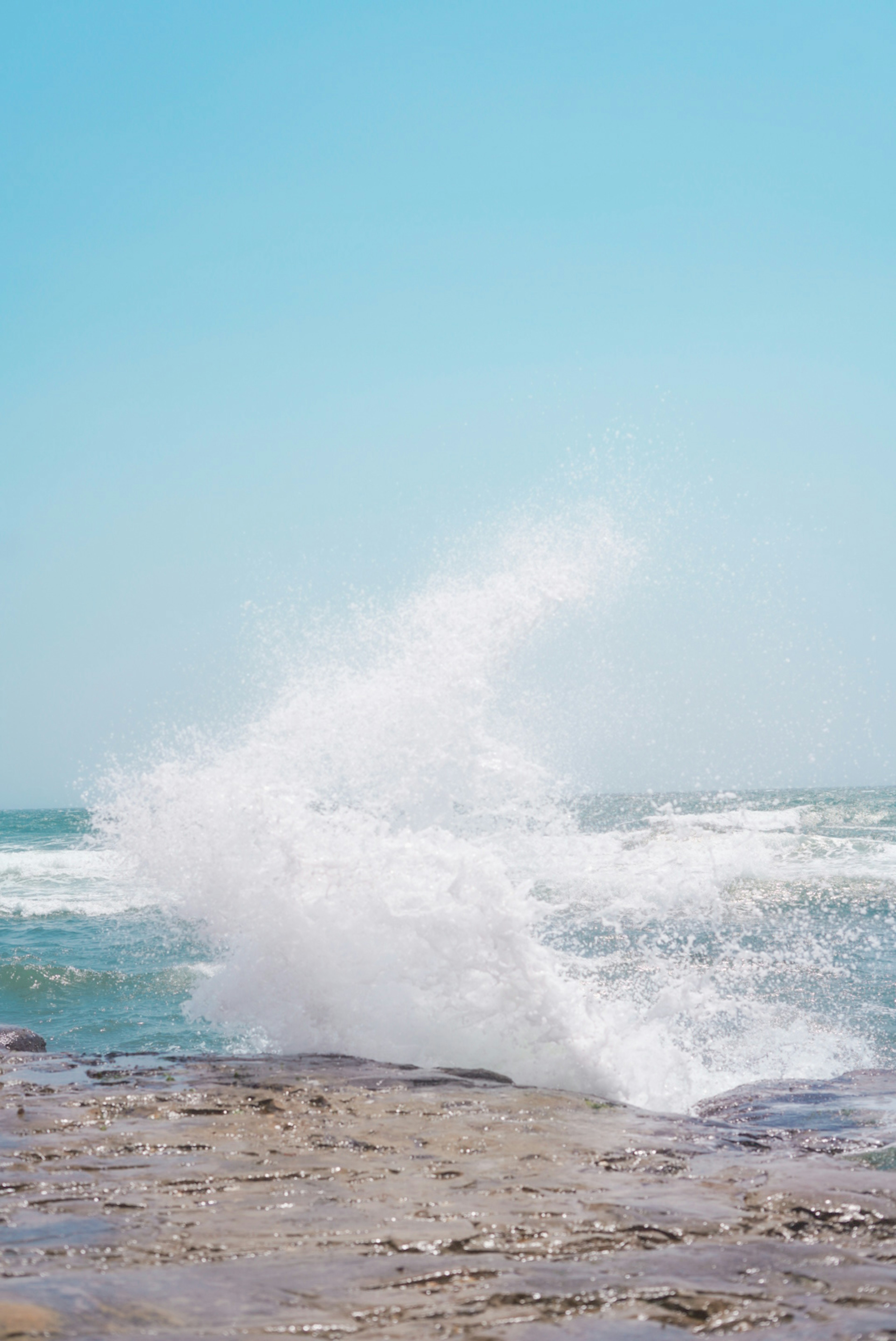 Onde del mare che si infrangono contro le rocce creando uno spruzzo sotto un cielo azzurro