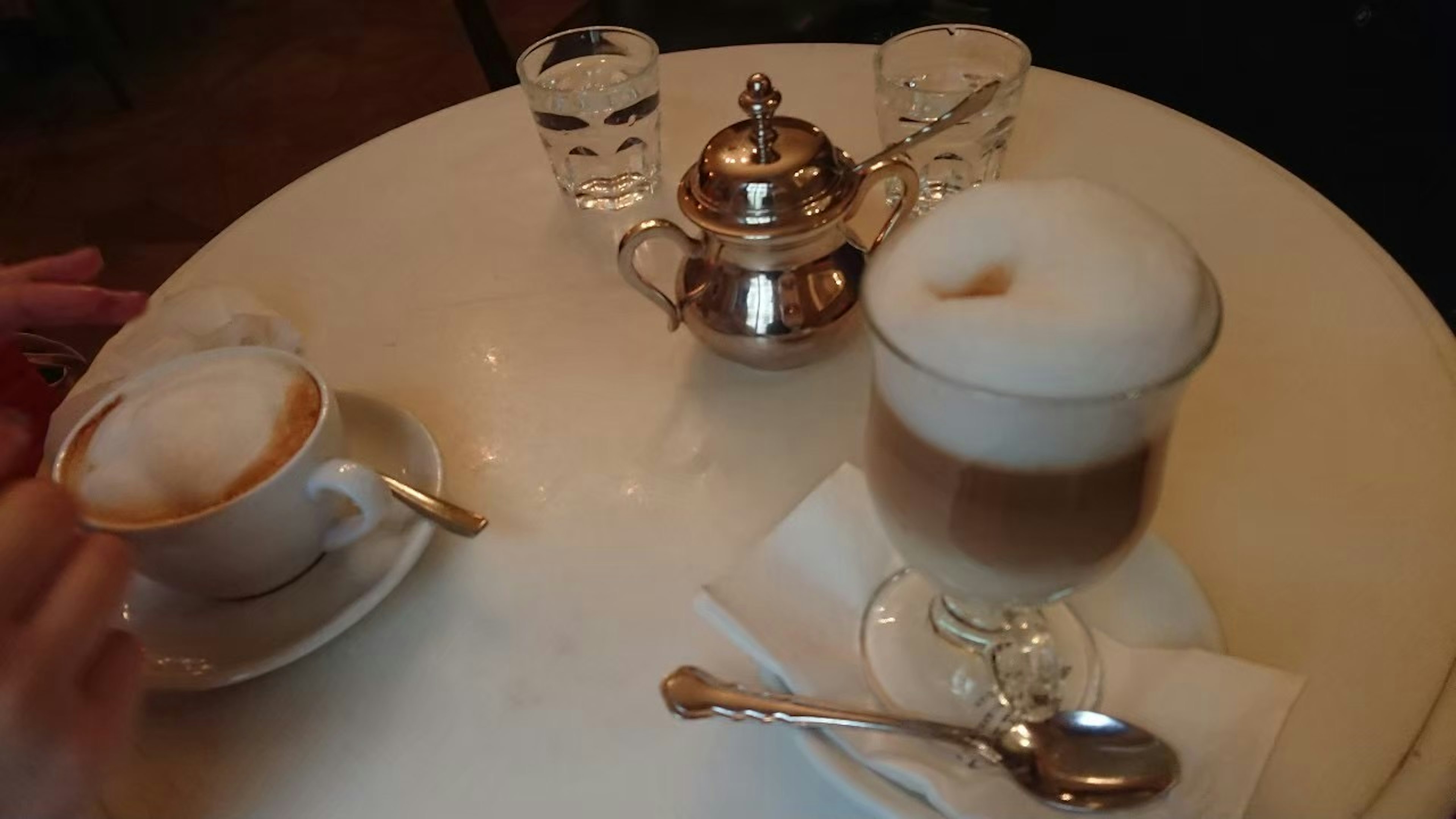 Configuración de mesa con una taza de capuchino y una taza de espresso con cobertura de leche espumosa tetera de plata y vasos transparentes