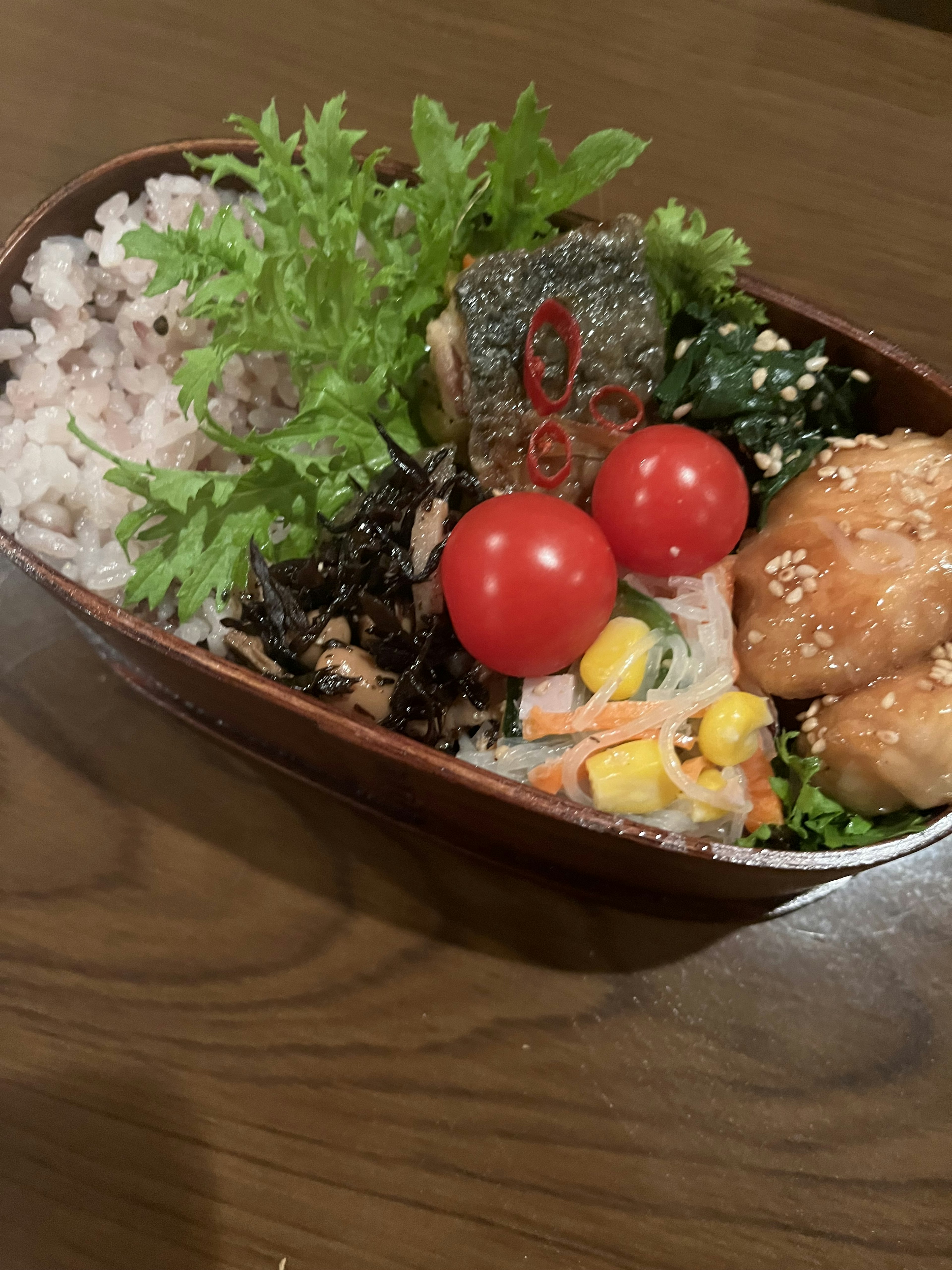 A beautifully arranged Japanese bento featuring rice, fish, vegetables, and cherry tomatoes