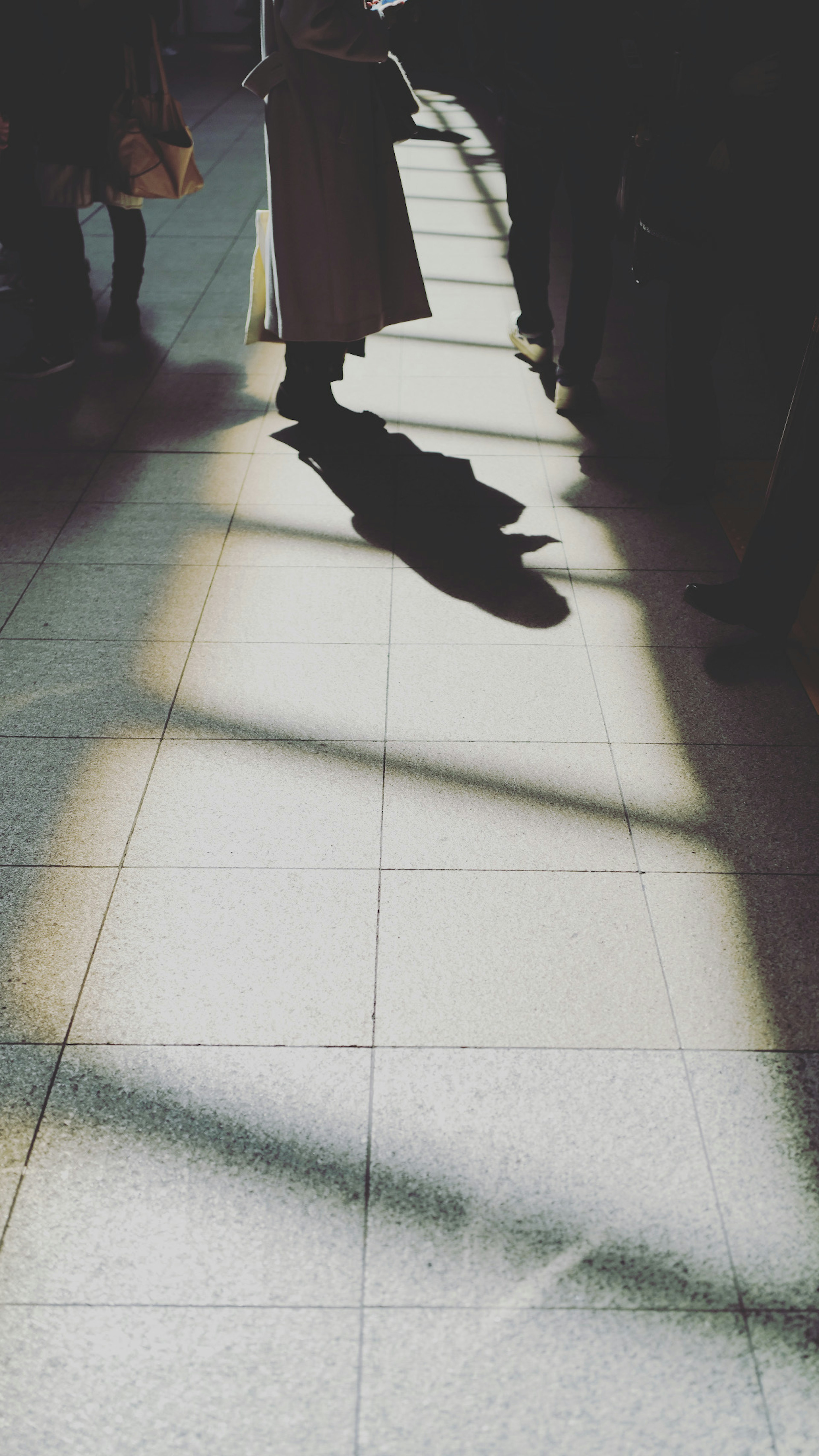 A person standing on the floor of a station with intersecting shadows and light