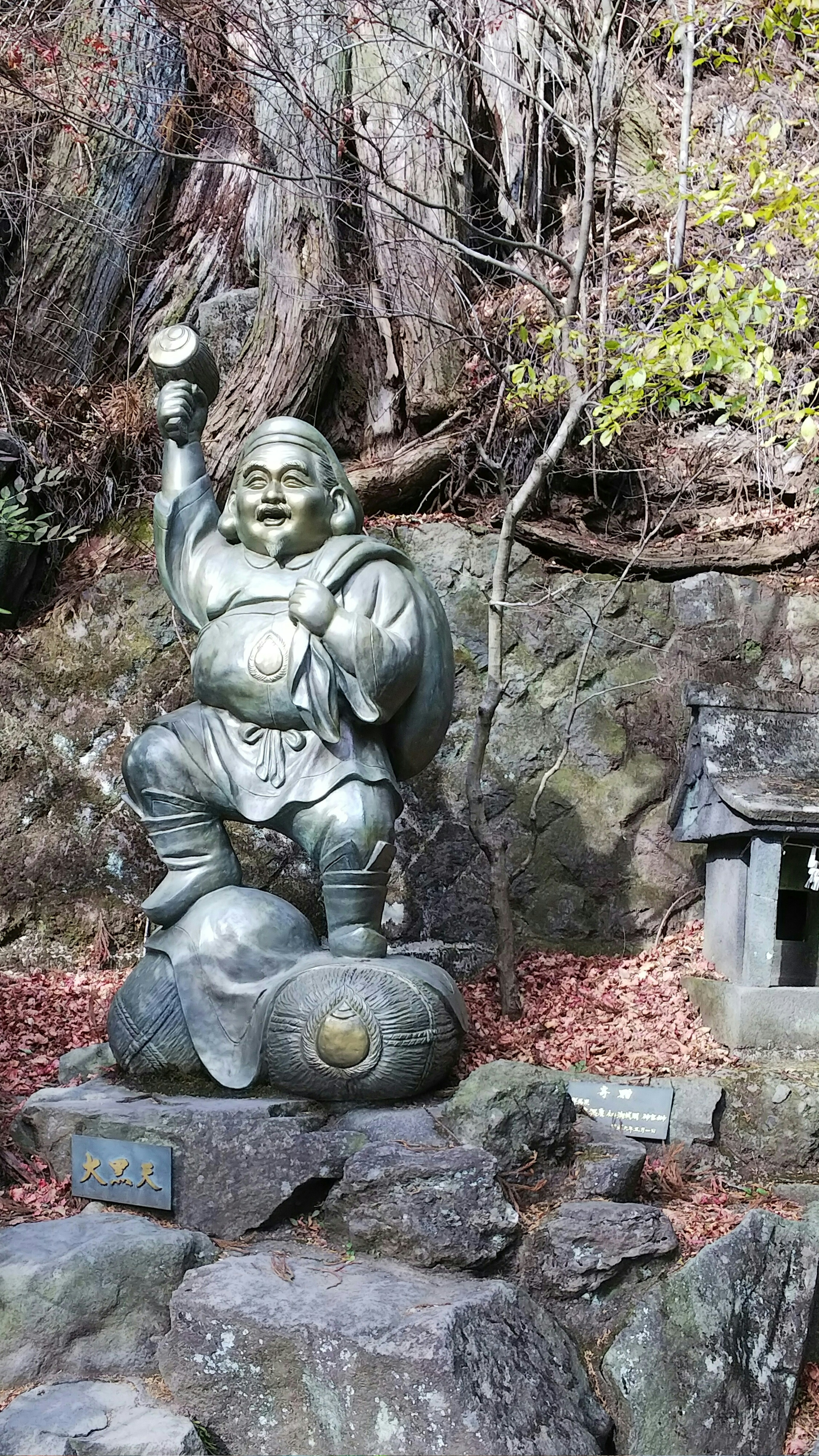 Una statua di una divinità fortunata si erge su una roccia, tenendo un lingotto d'oro con un sorriso