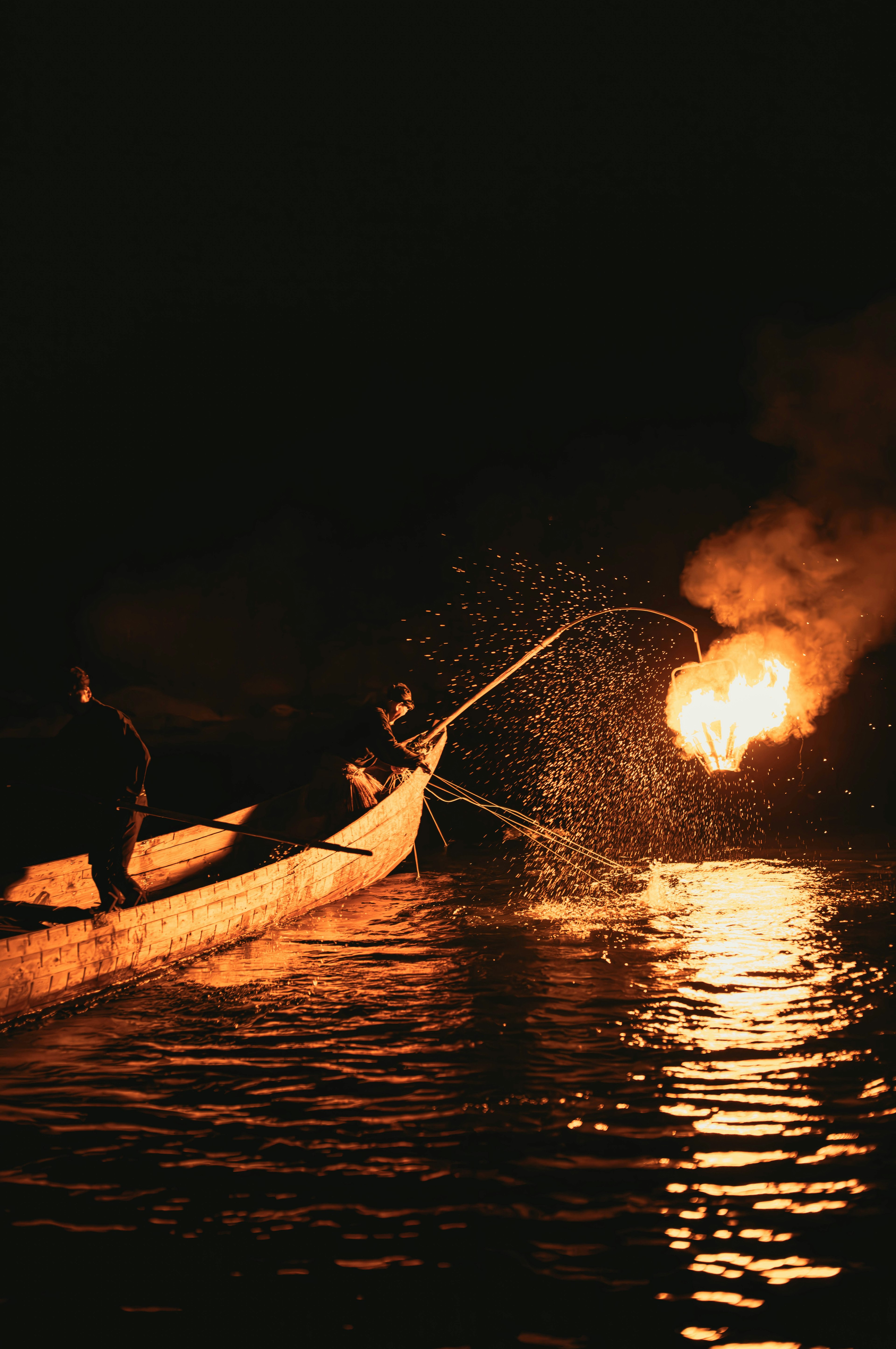 Nelayan di perahu di malam hari dengan api dan percikan air