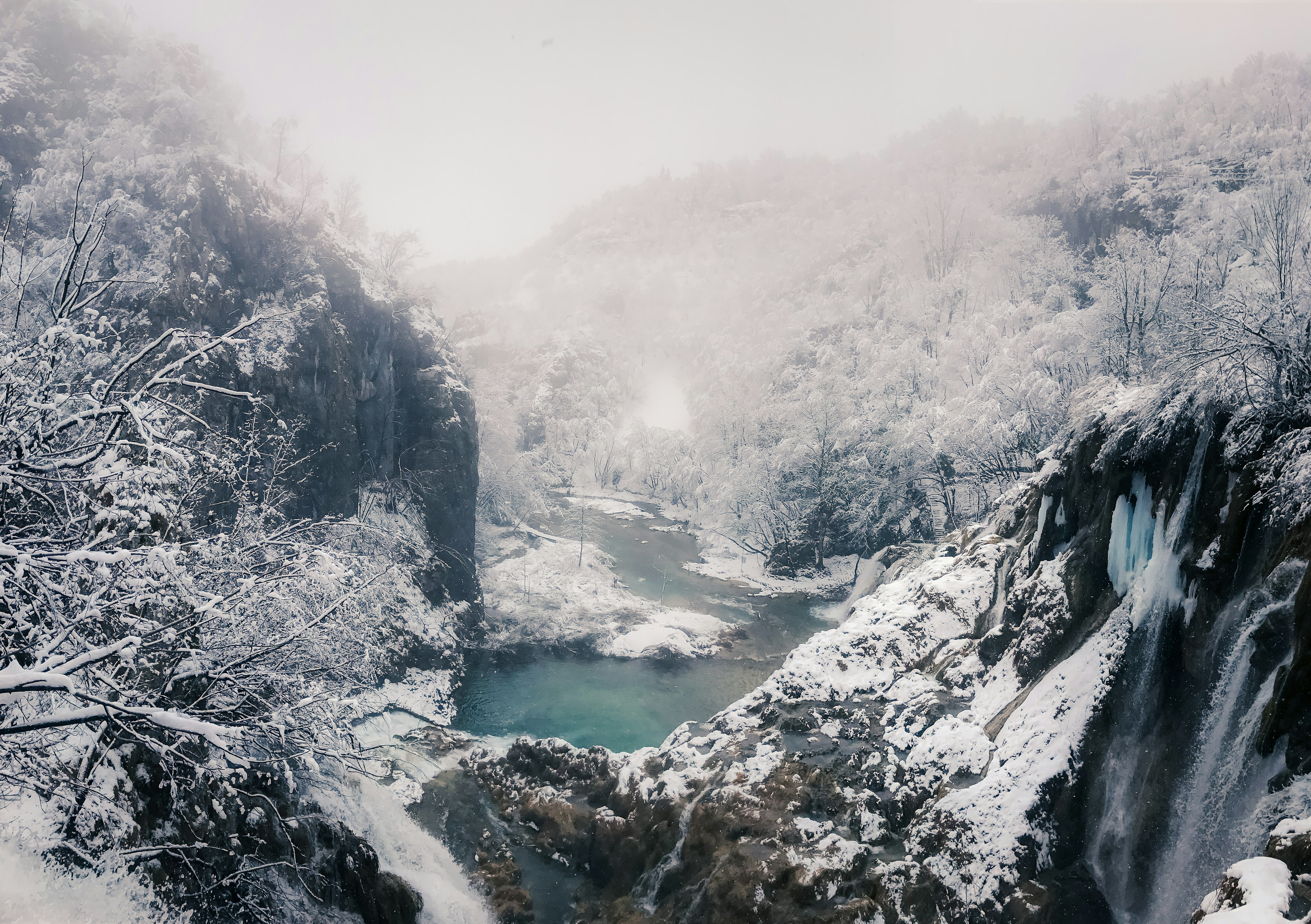 Verschneite Tal mit Wasserfällen und einem kalten blauen Fluss