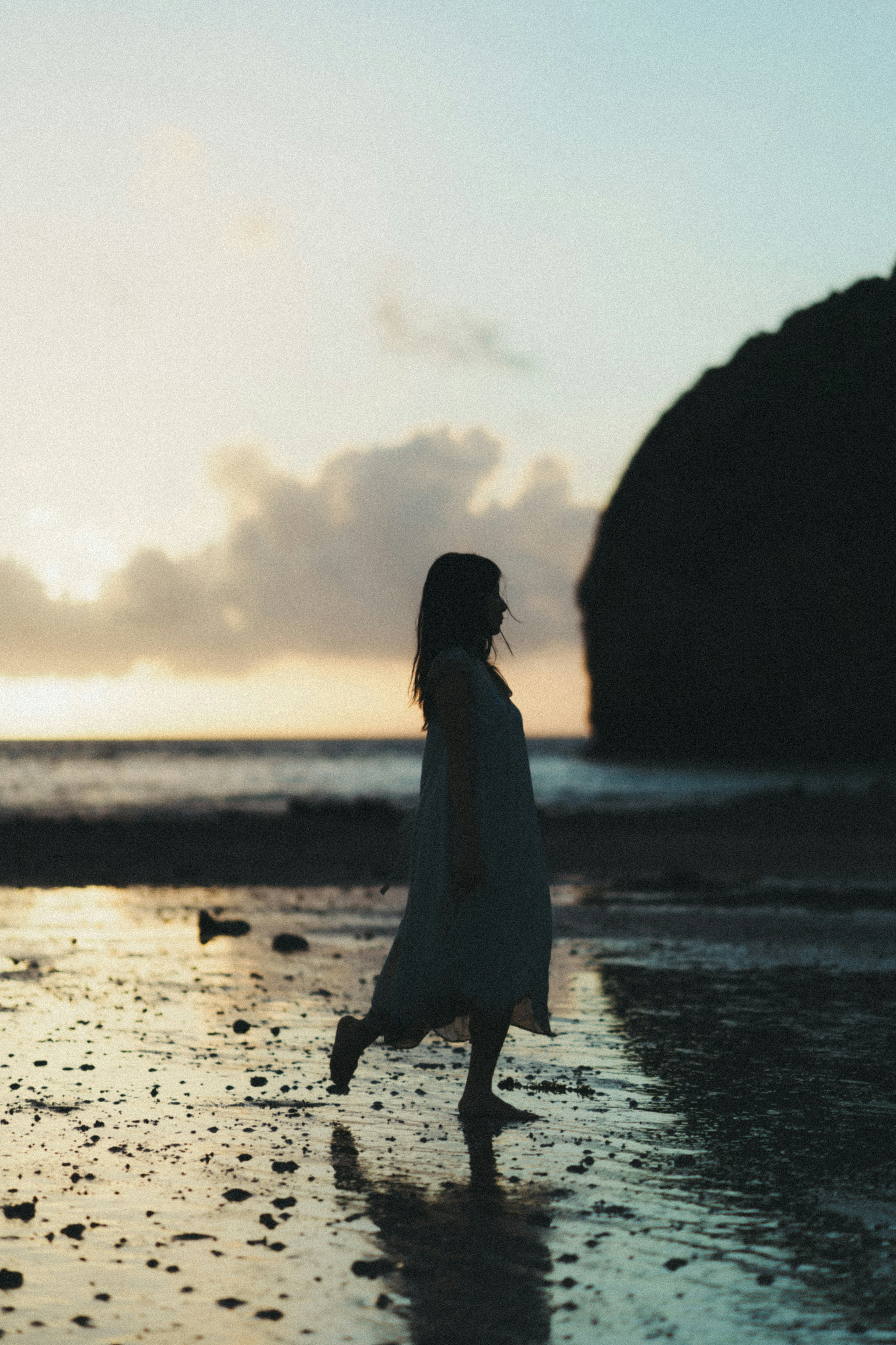 Siluet seorang wanita berjalan di pantai saat matahari terbenam