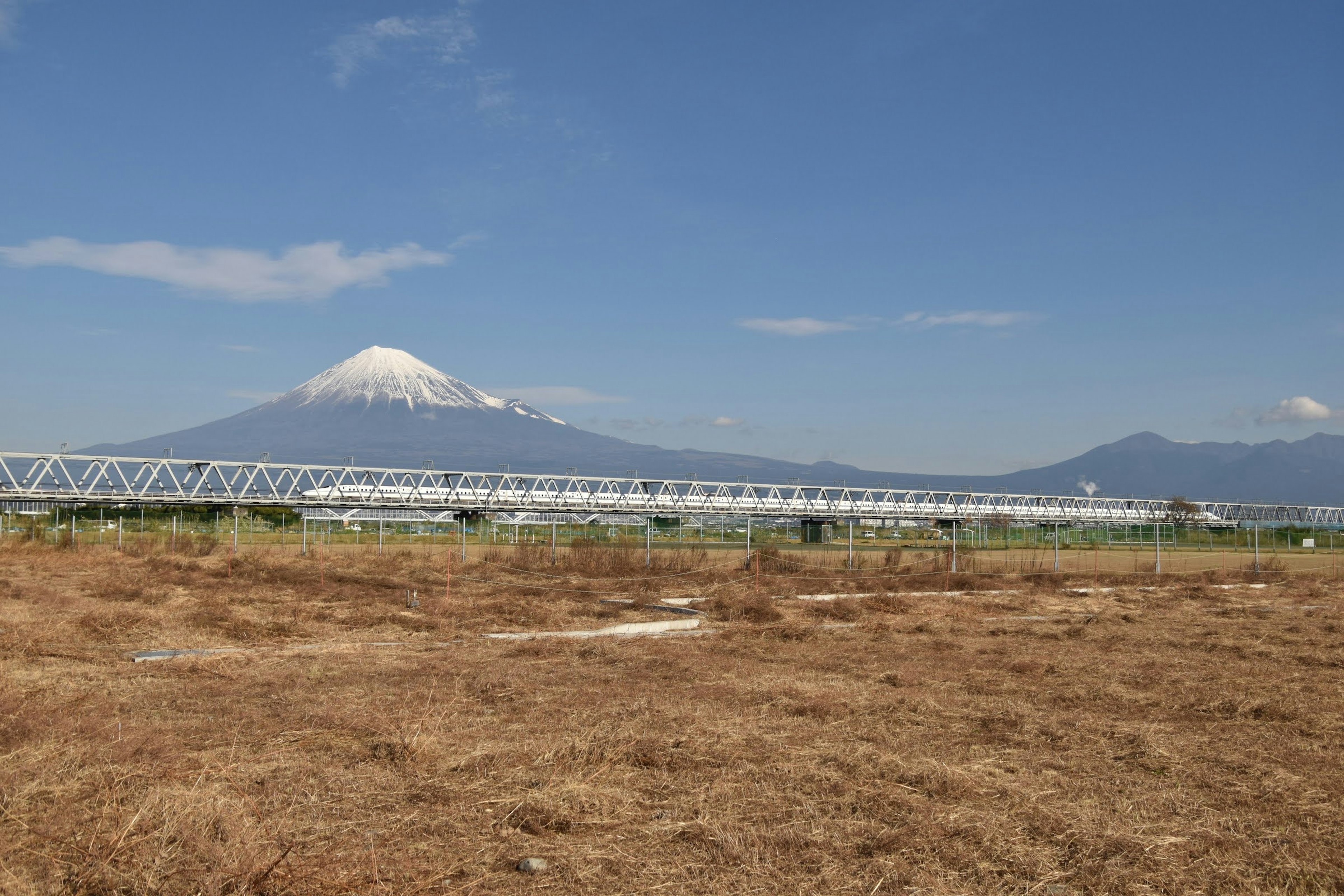 富士山が背景に広がる乾燥した草原と鉄道の風景