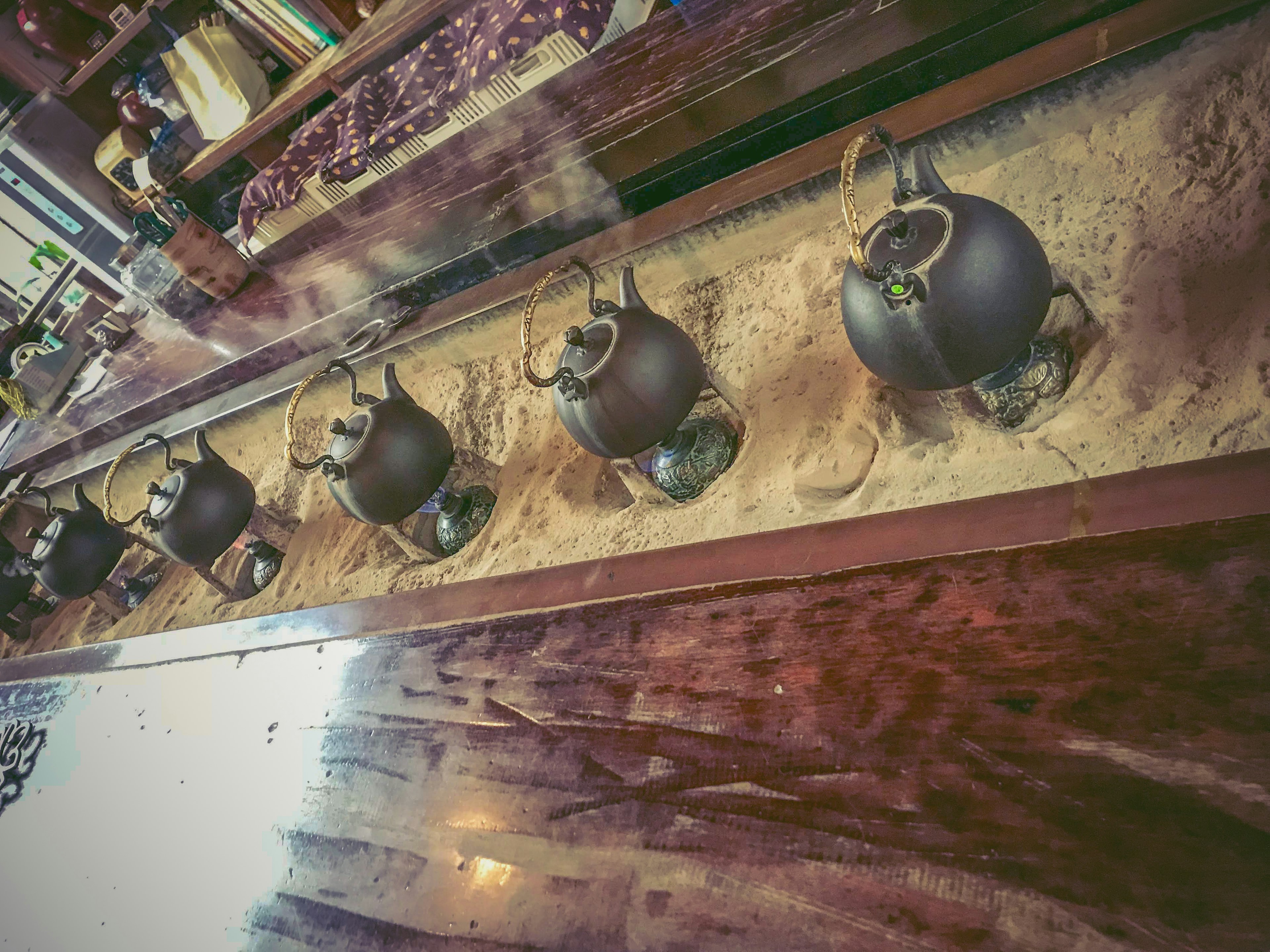 A row of black ceramic teapots on a wooden table with sand