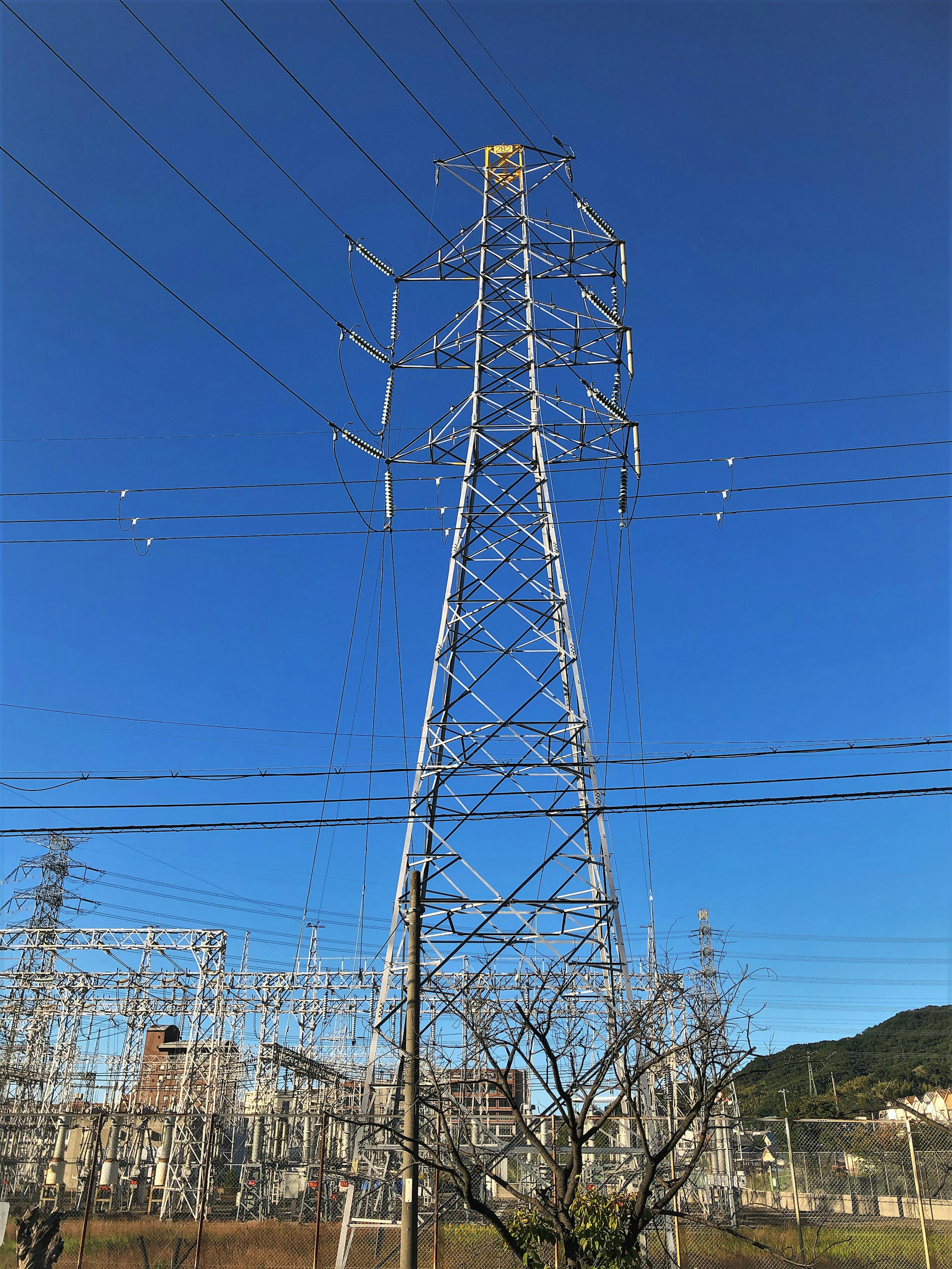 High voltage power tower under clear blue sky near electrical infrastructure