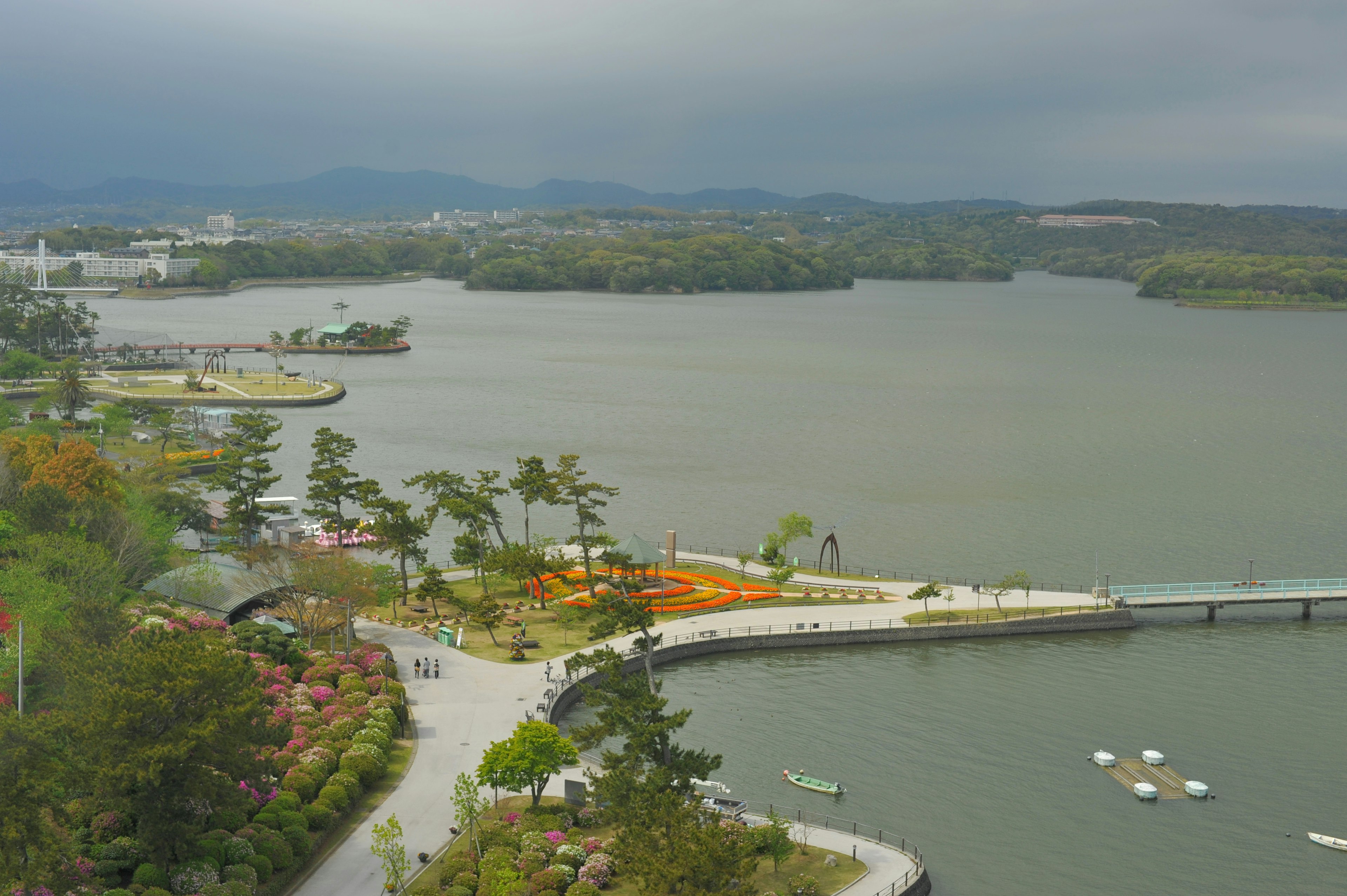 Landschaftlicher Blick auf einen ruhigen See mit Grünflächen und einem Park mit einer Brücke und Booten