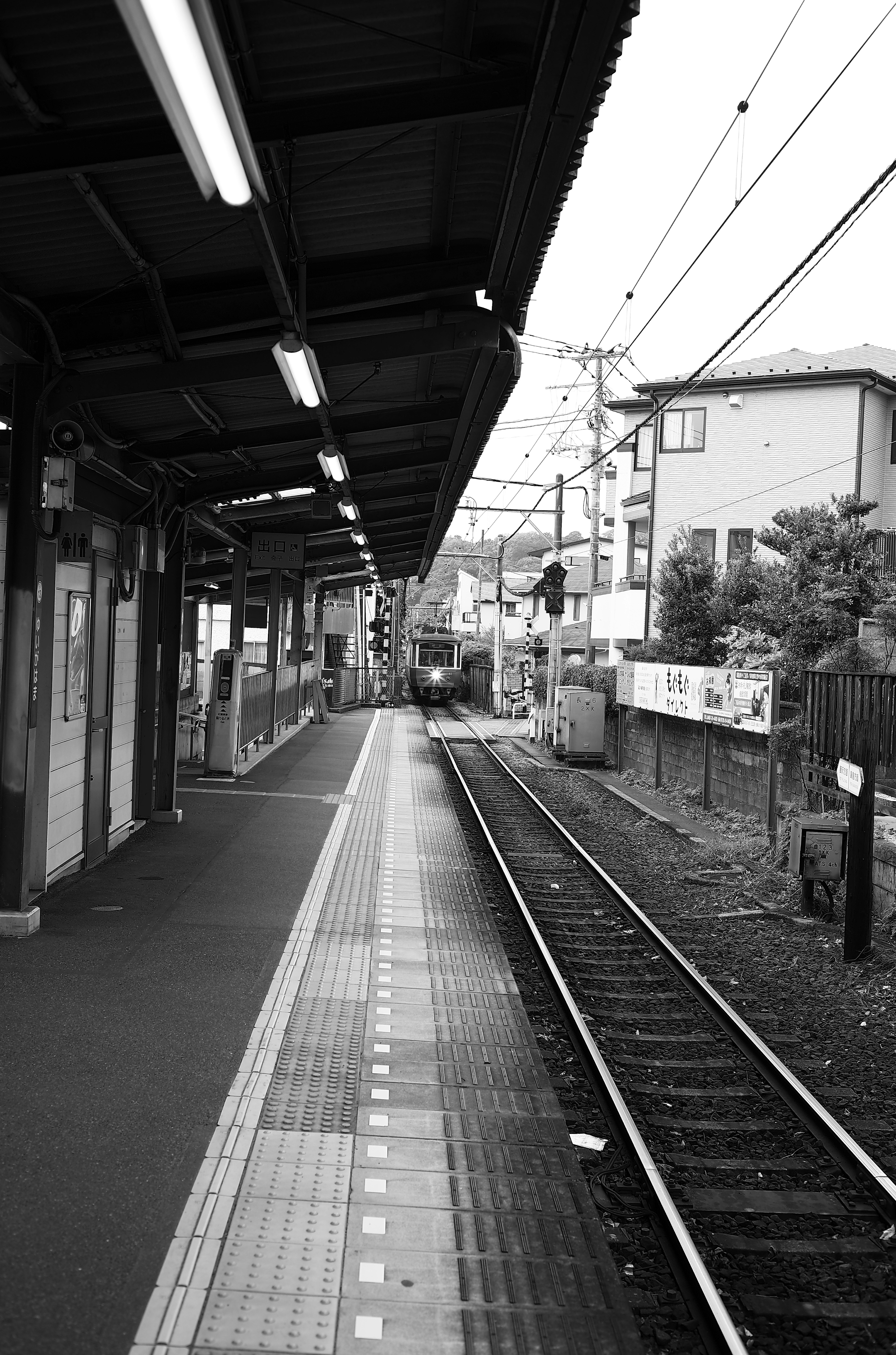 A quiet train station platform with tracks in black and white