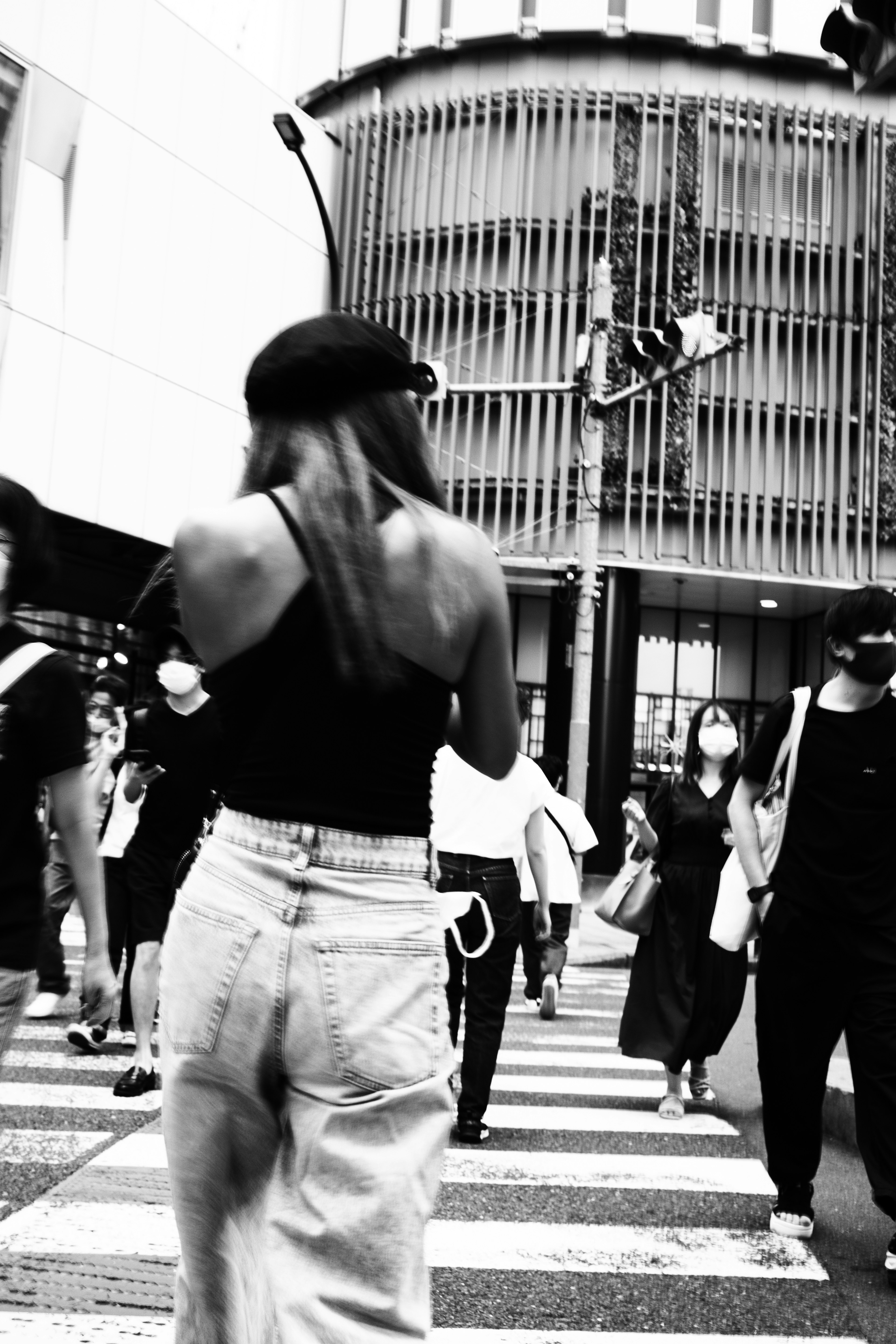 A woman in a black top and white pants walking at a crosswalk in an urban setting