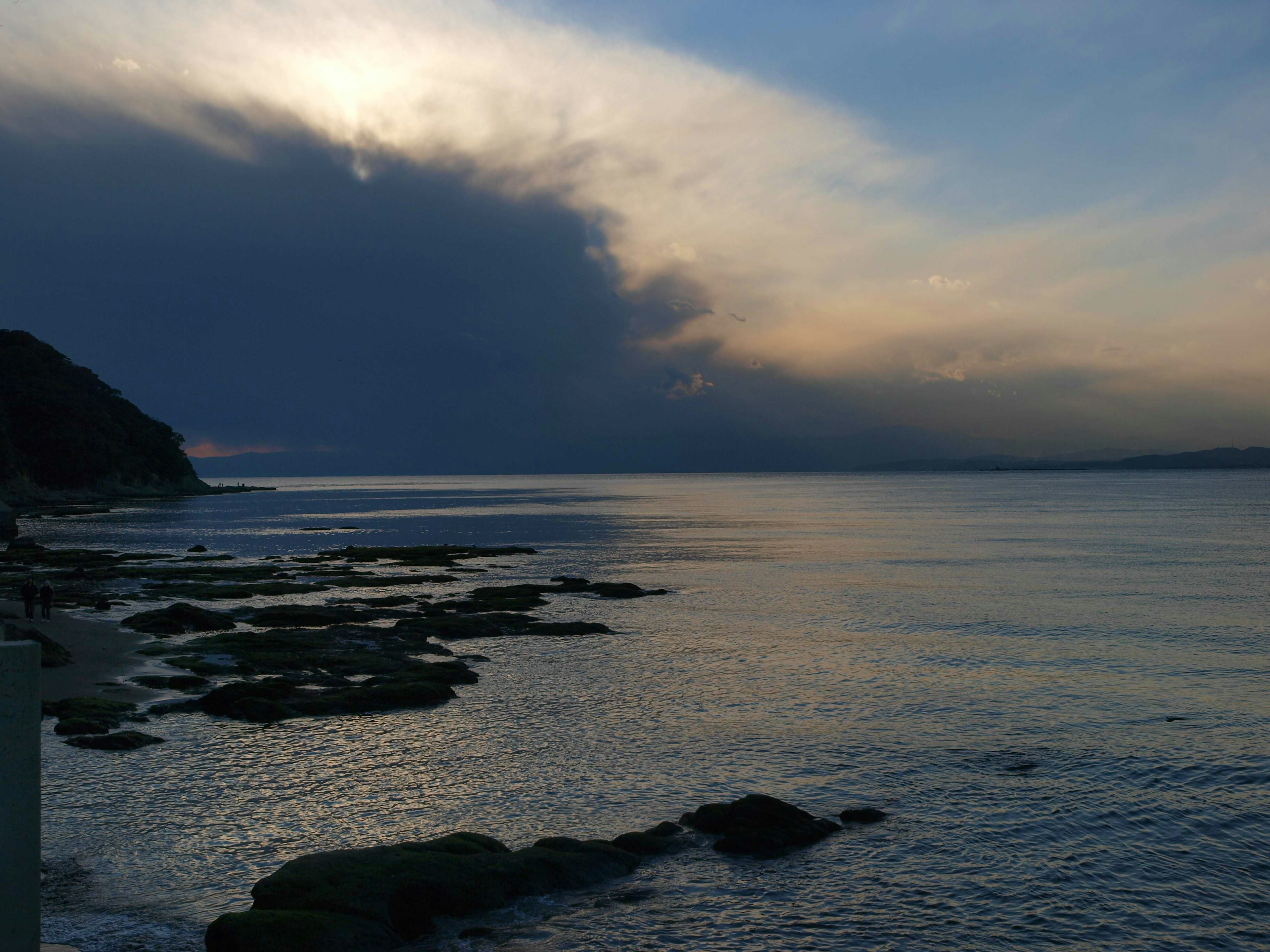 Pemandangan pantai dengan batuan dan air tenang di bawah awan gelap