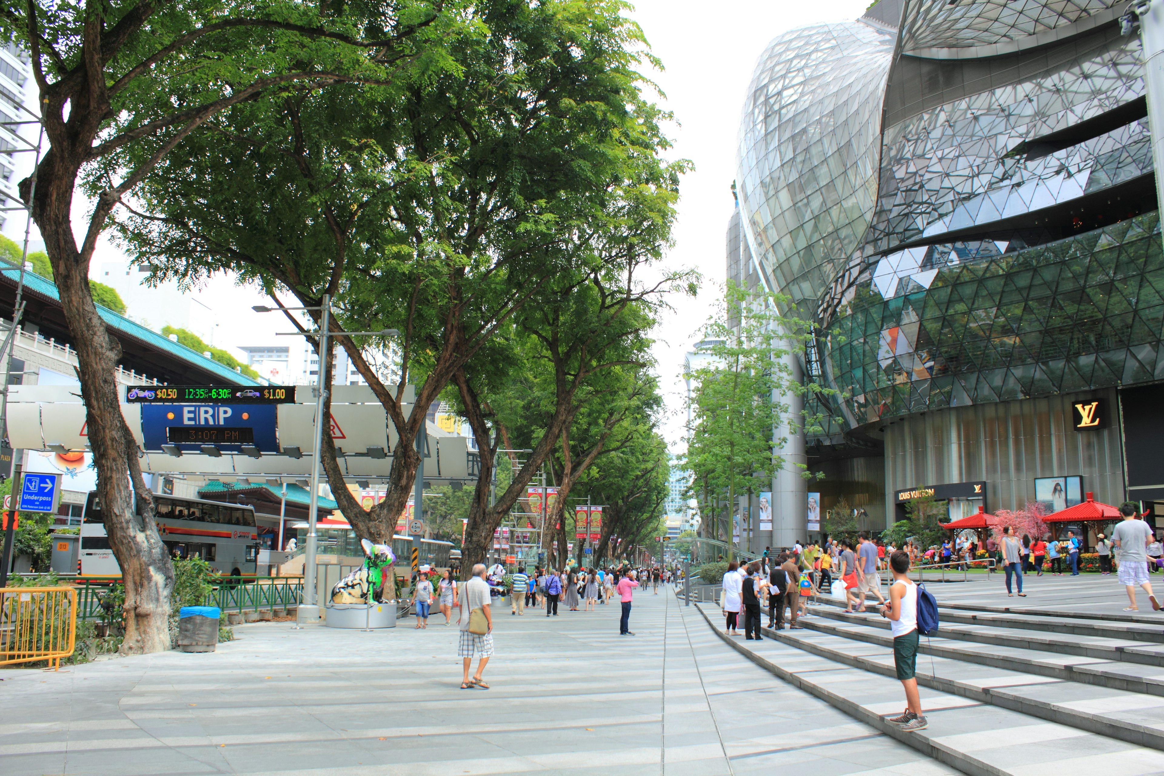 A busy street lined with green trees and modern buildings