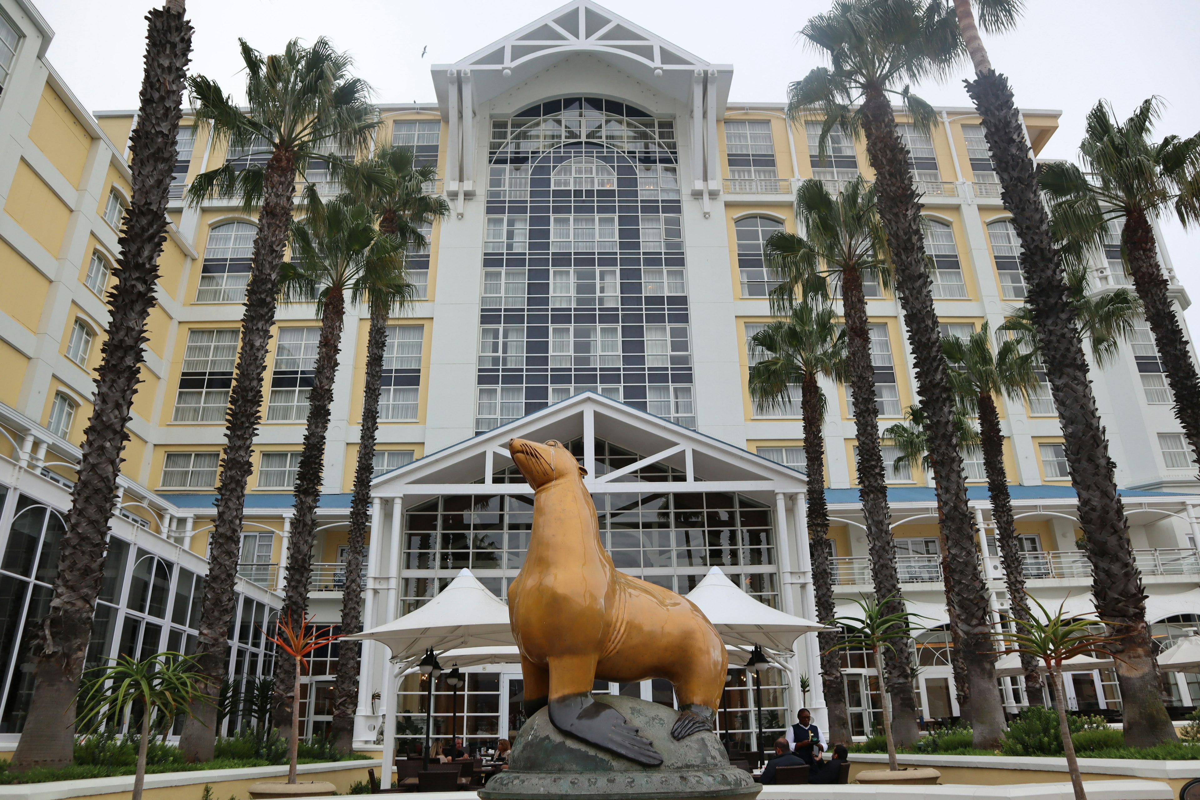 Fasad hotel dengan patung anjing laut besar dan pohon palem