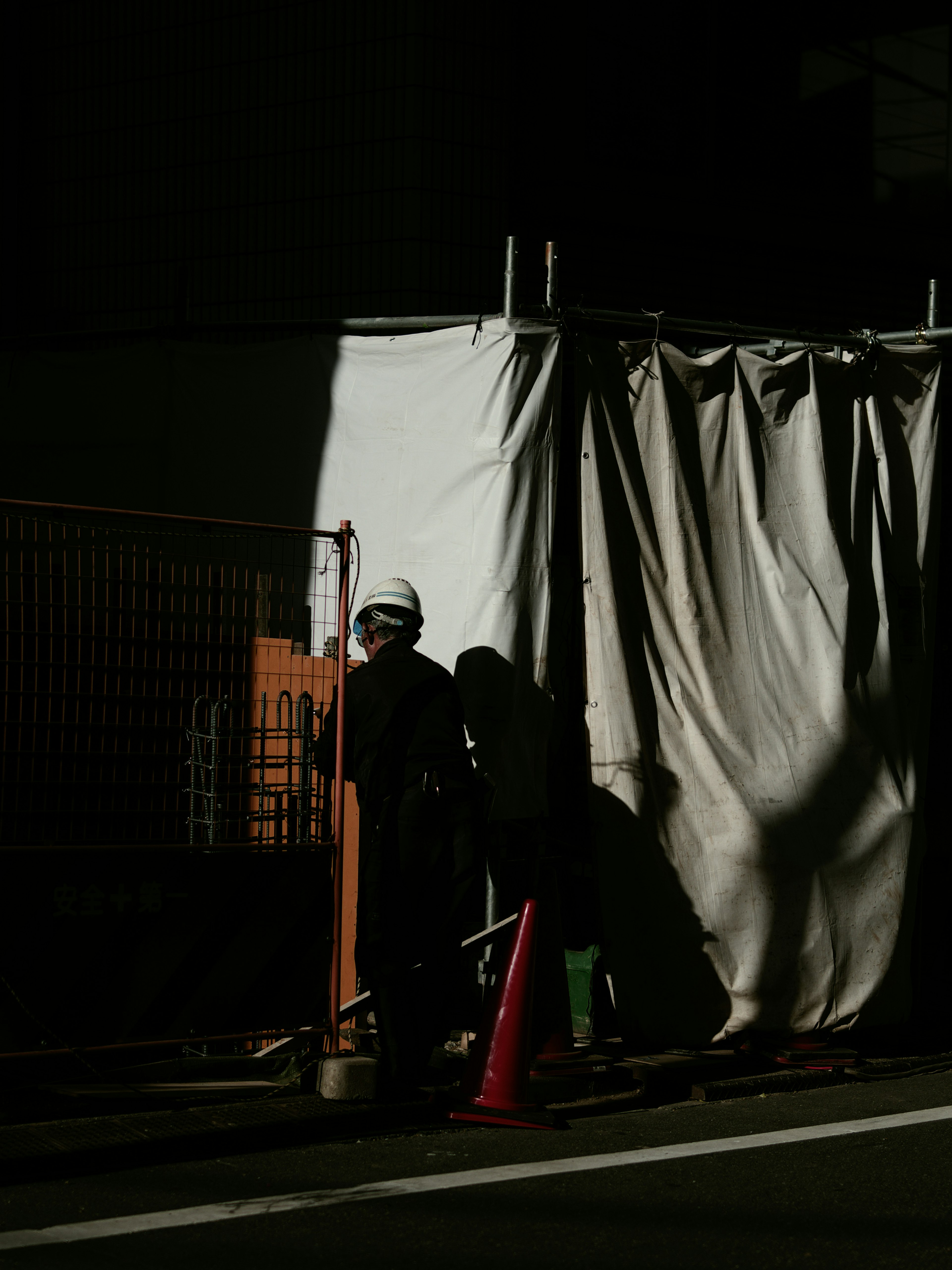 Arbeiter im Schatten neben der weißen Vorhangstruktur