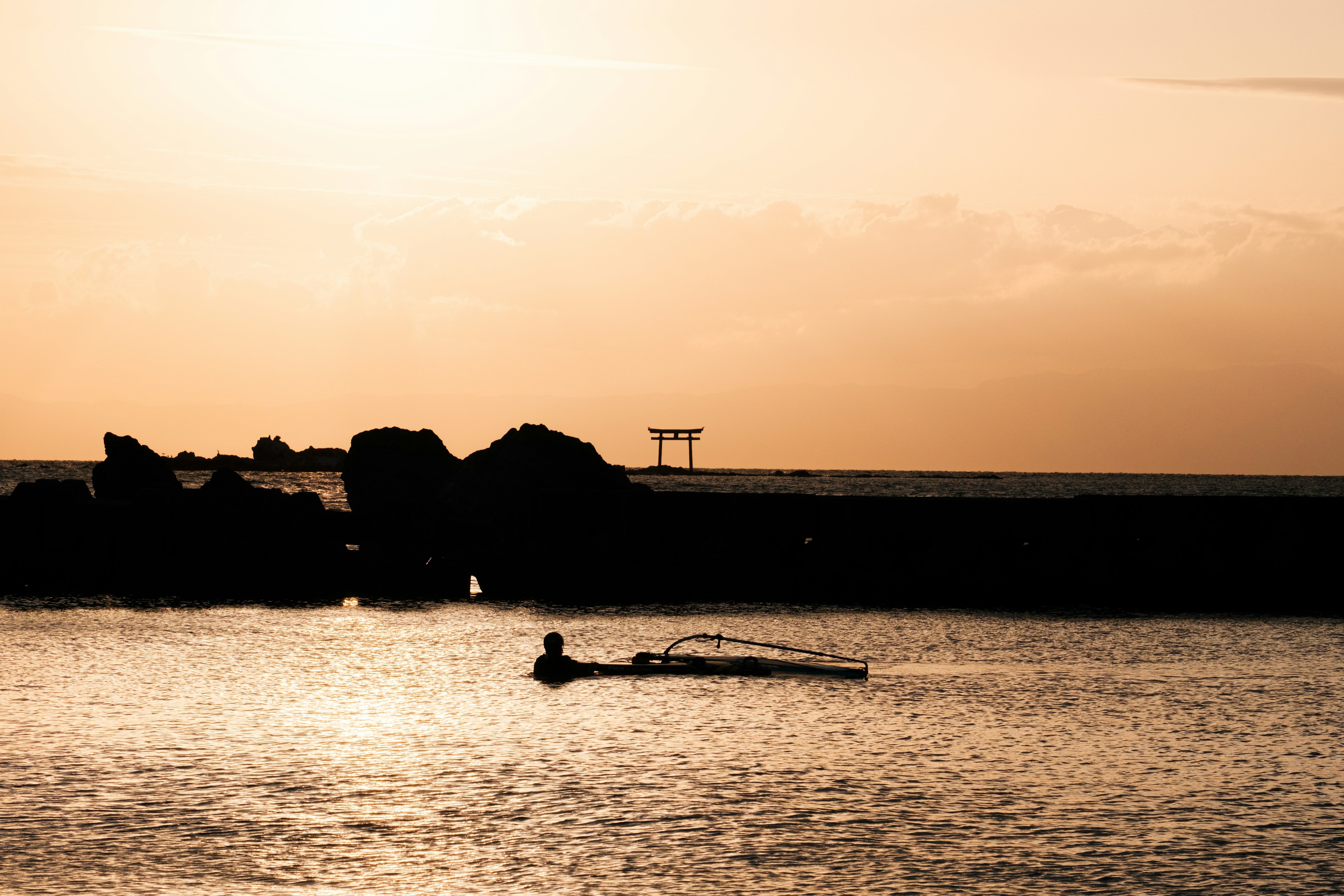 夕焼けの海で漁をする漁師のシルエットと岩の風景