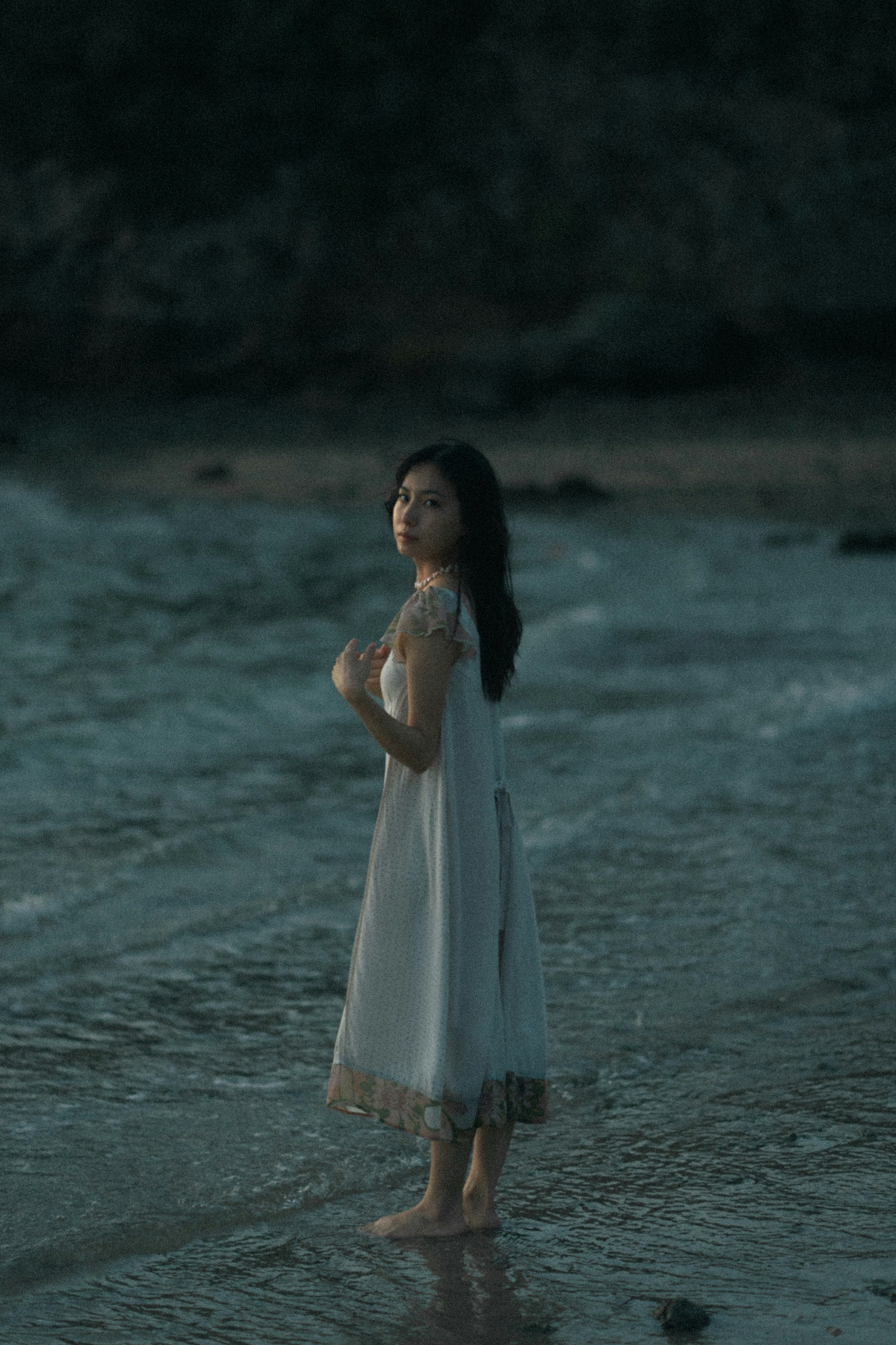 Una mujer con un vestido blanco de pie junto a la orilla