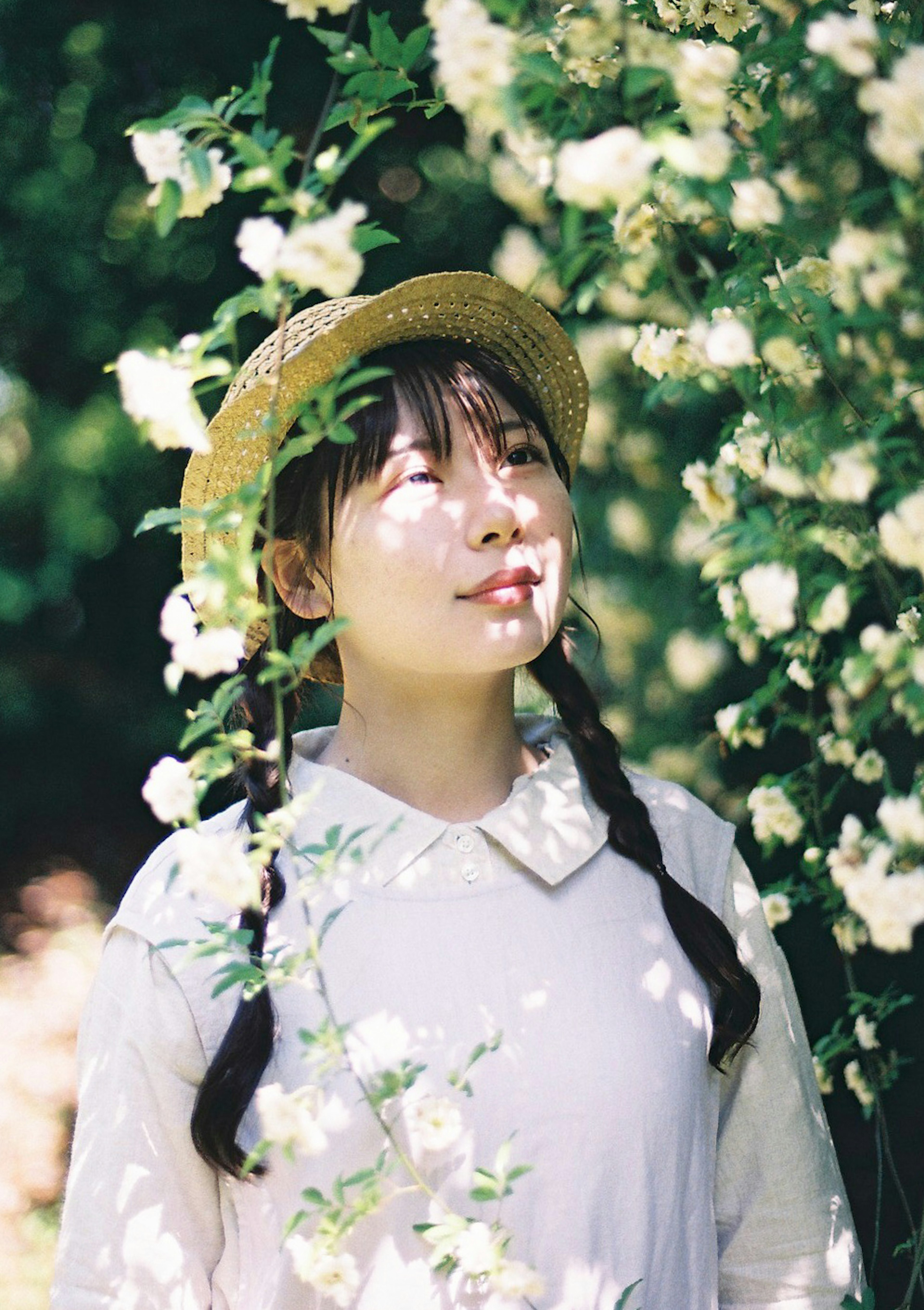 Portrait d'une femme souriante parmi des fleurs portant un chapeau de paille et une robe blanche