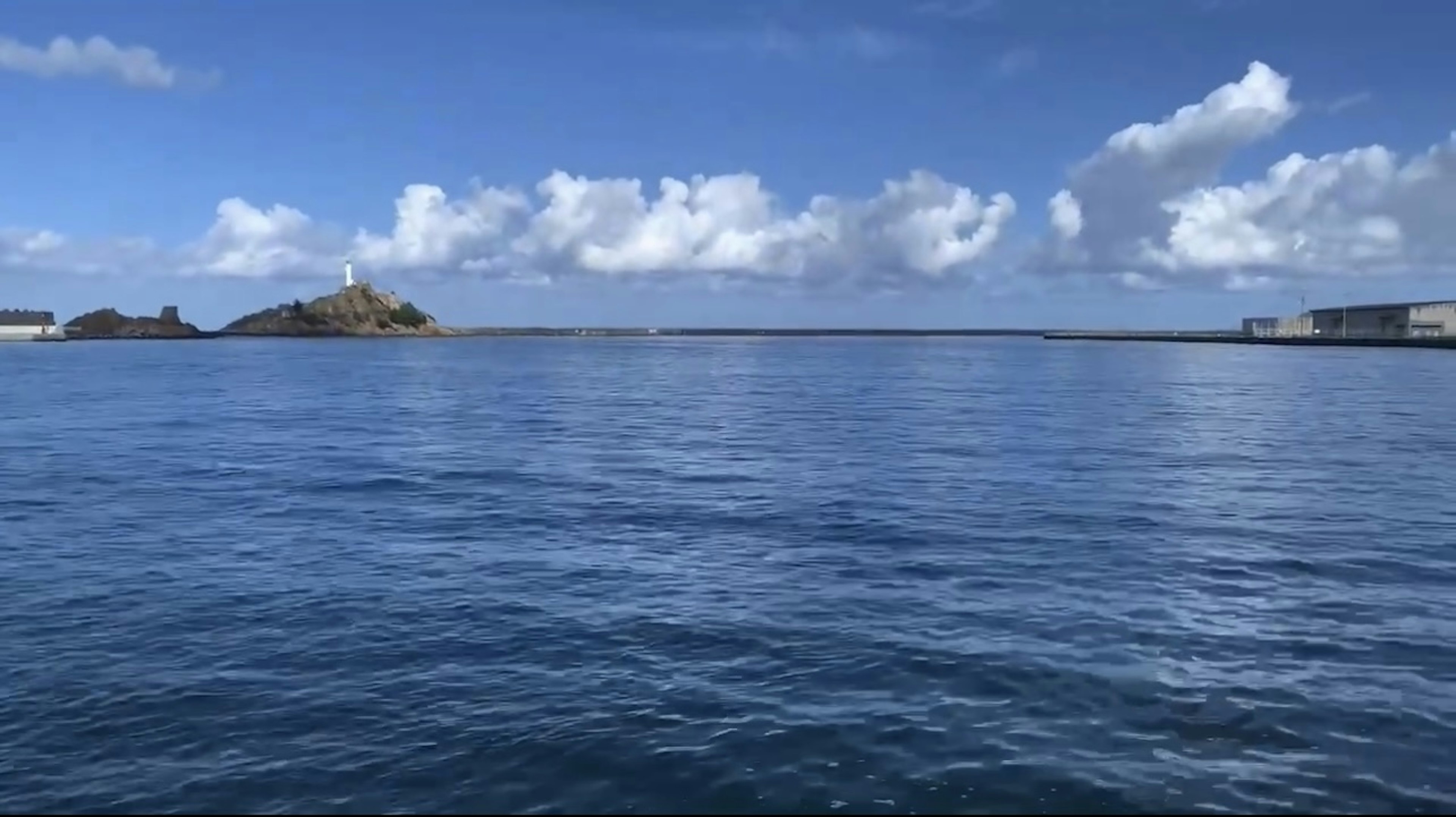 A scenic view featuring a small island with a lighthouse under a blue sky and calm ocean