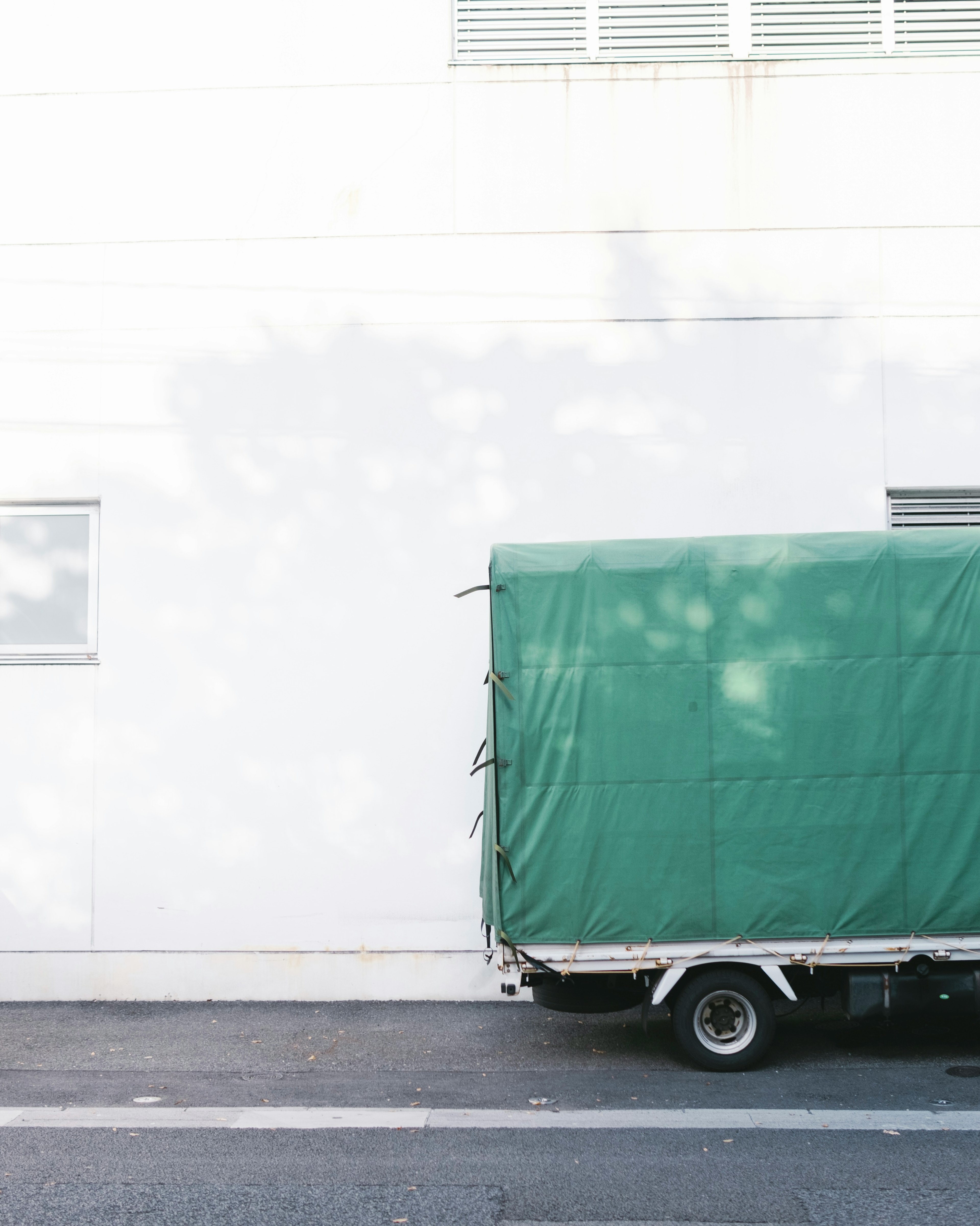 Green covered truck parked beside a white wall