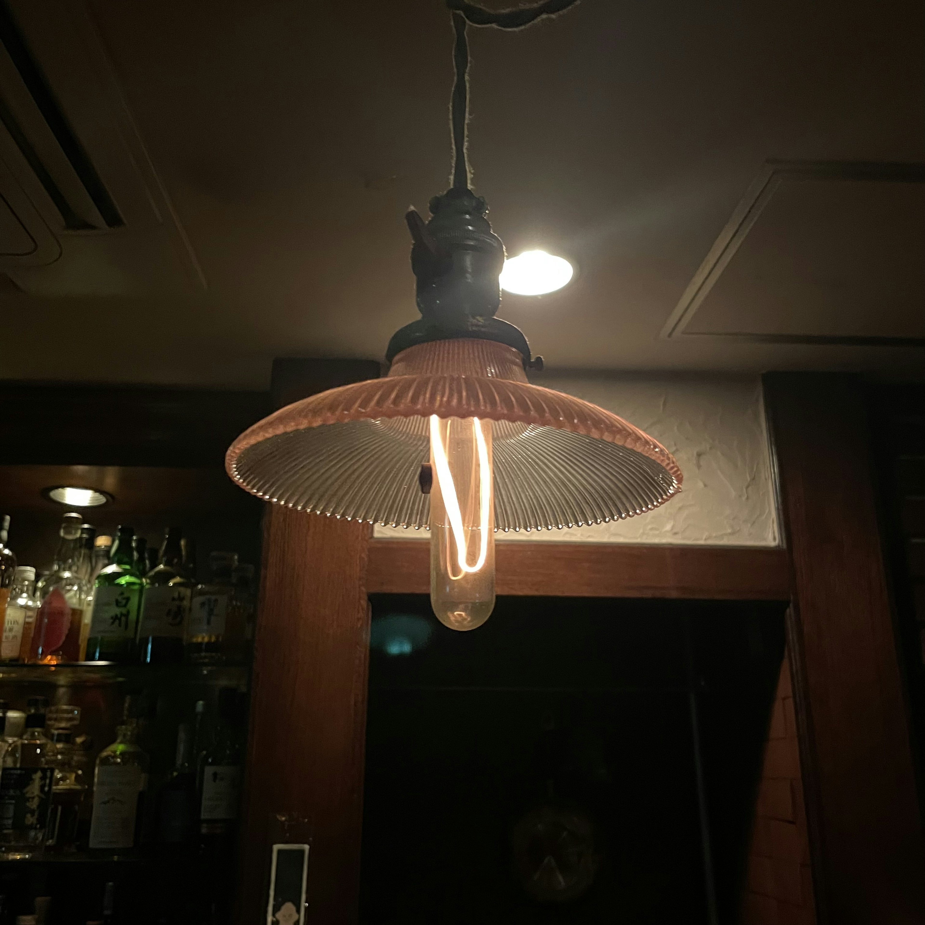 Sebuah lampu retro yang memancarkan cahaya hangat menggantung di atas meja bar