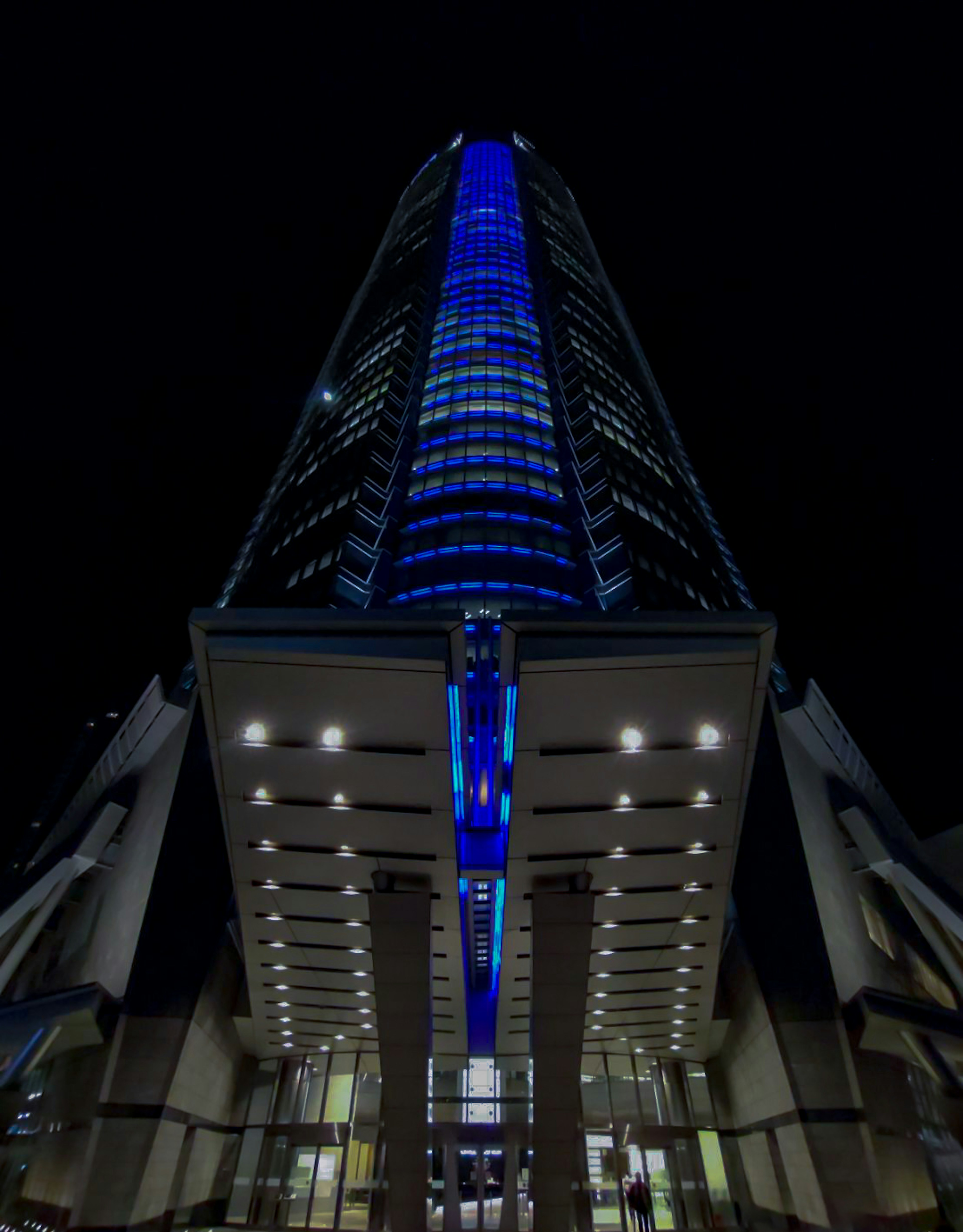 Blick von unten auf ein hohes Gebäude, das nachts mit blauen Lichtern beleuchtet ist