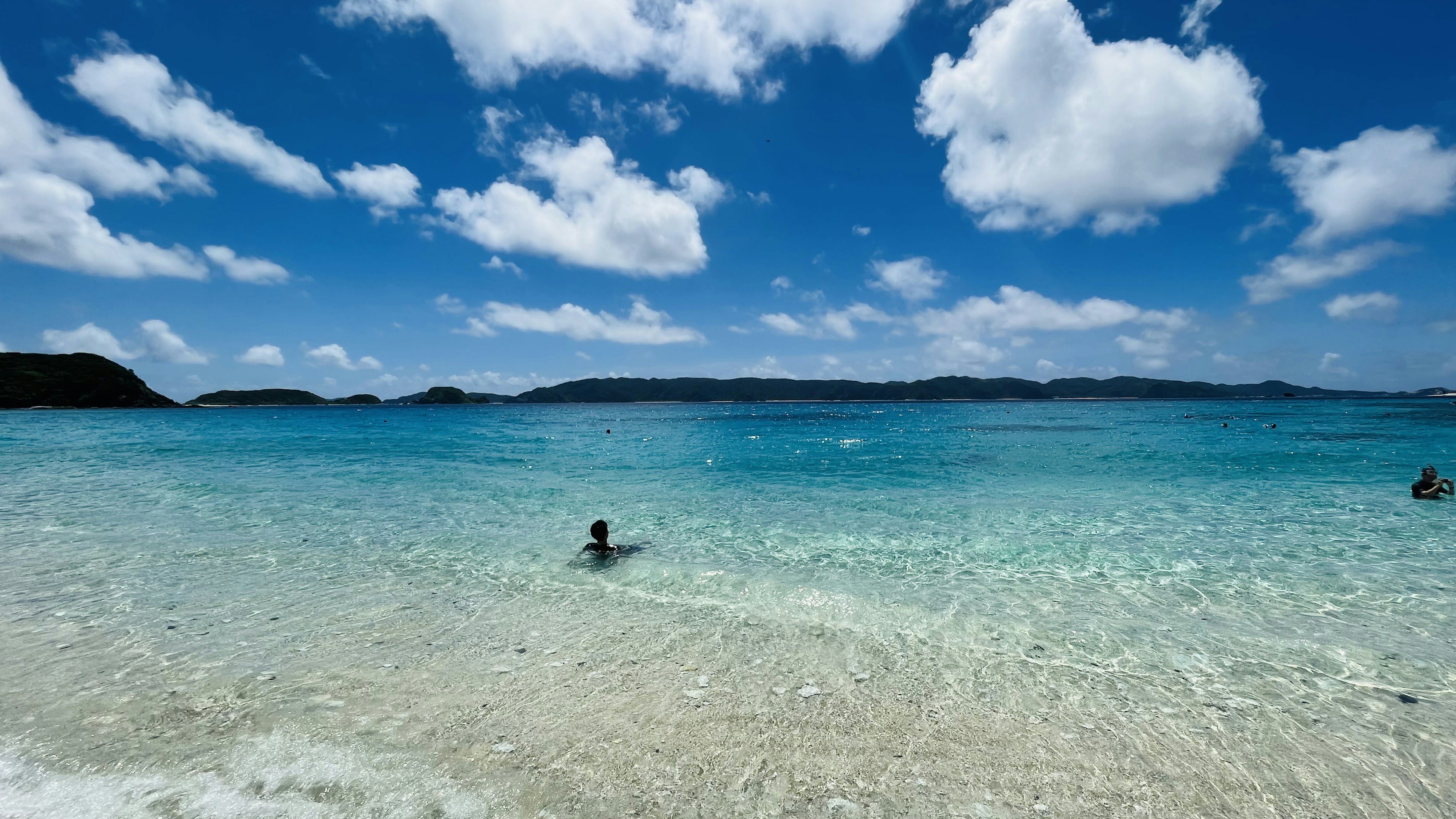 透き通った青い海と白い砂浜の風景に人が泳いでいる