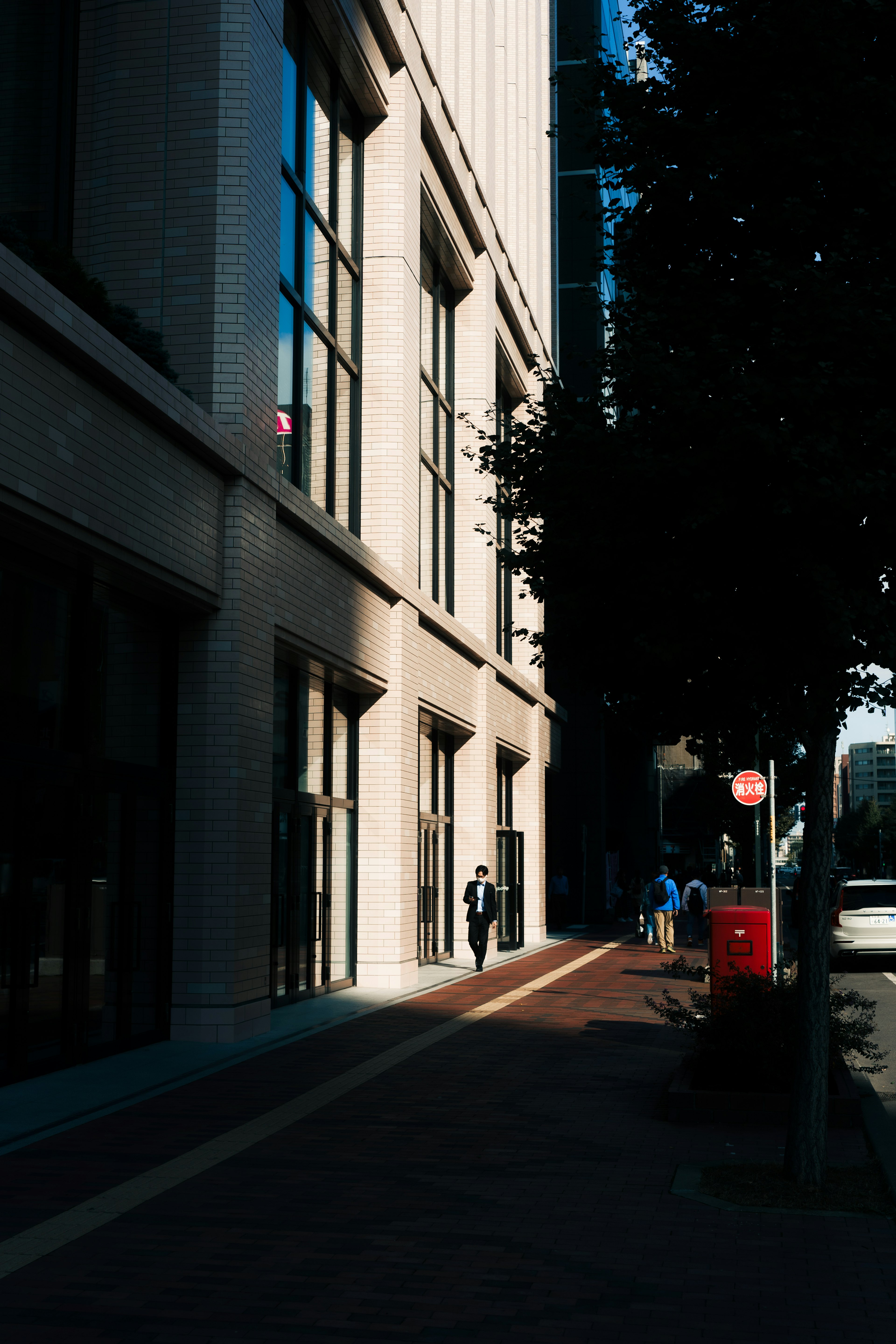 Vista de la acera de un edificio alto con sombras y una persona caminando