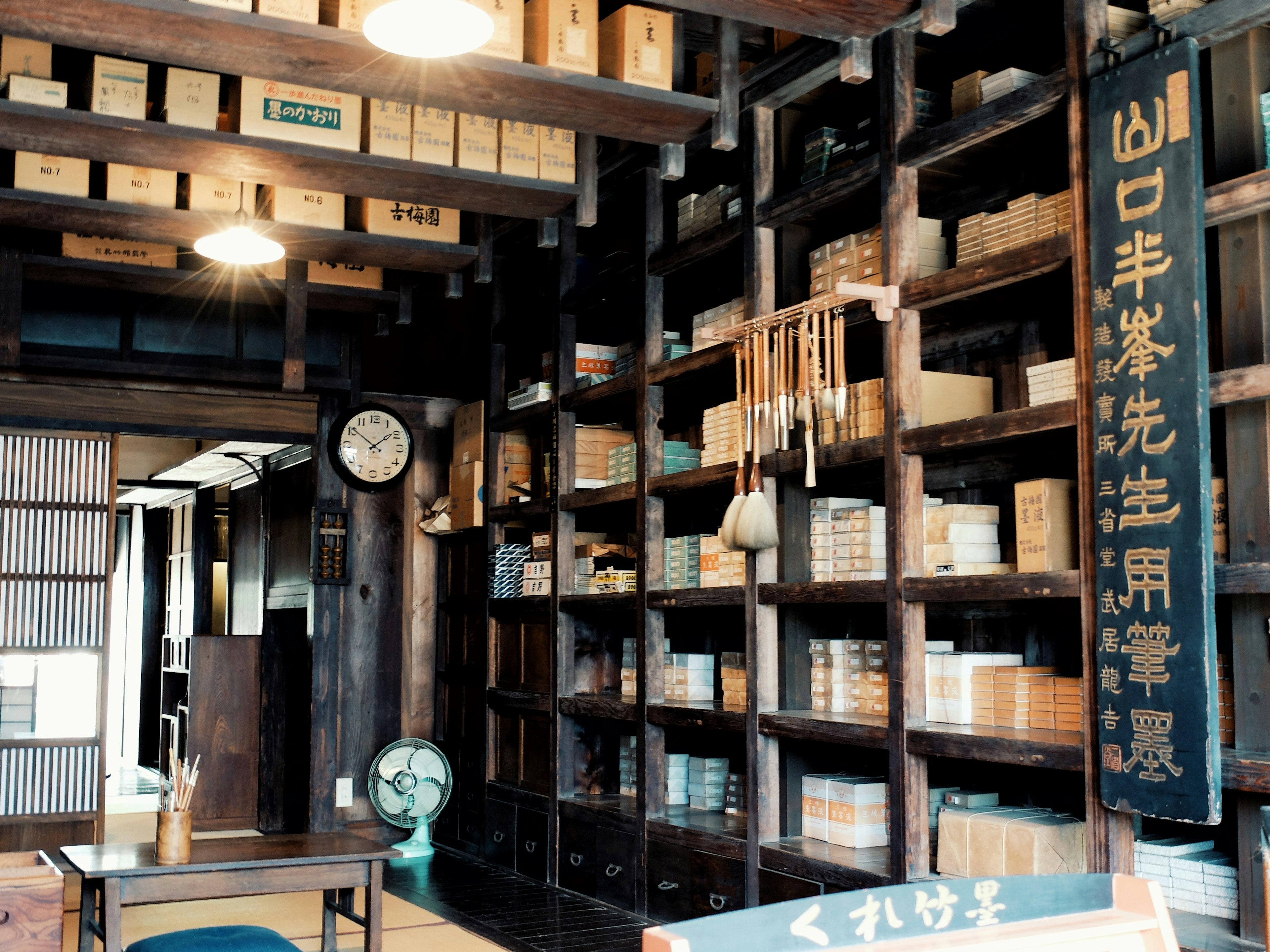 Traditional Japanese shop interior with wooden shelves filled with neatly arranged boxes an old sign on the wall a clock and a fan visible