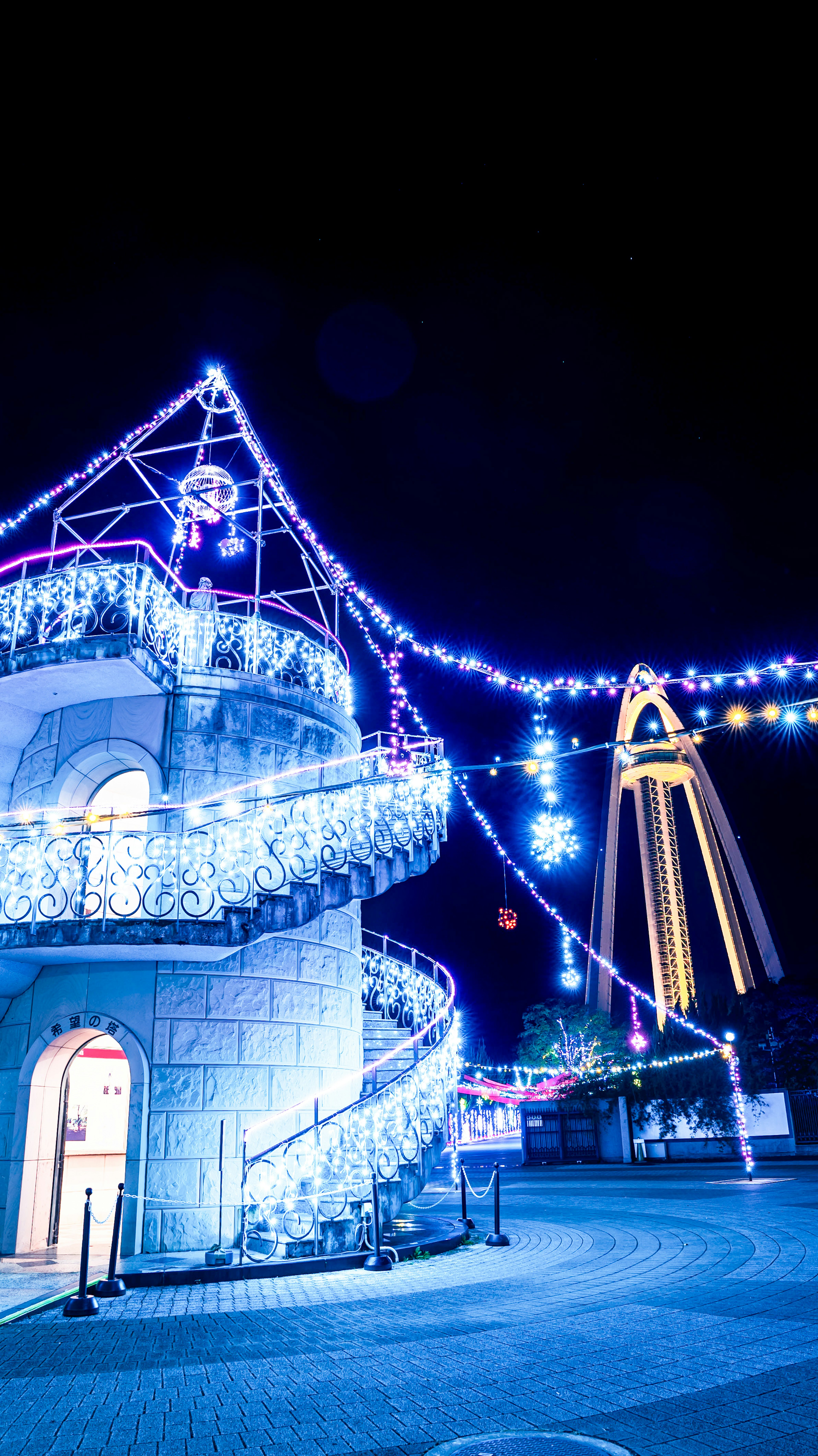 Lumières bleues illuminées sur un escalier en spirale avec une grande structure en arc en arrière-plan la nuit