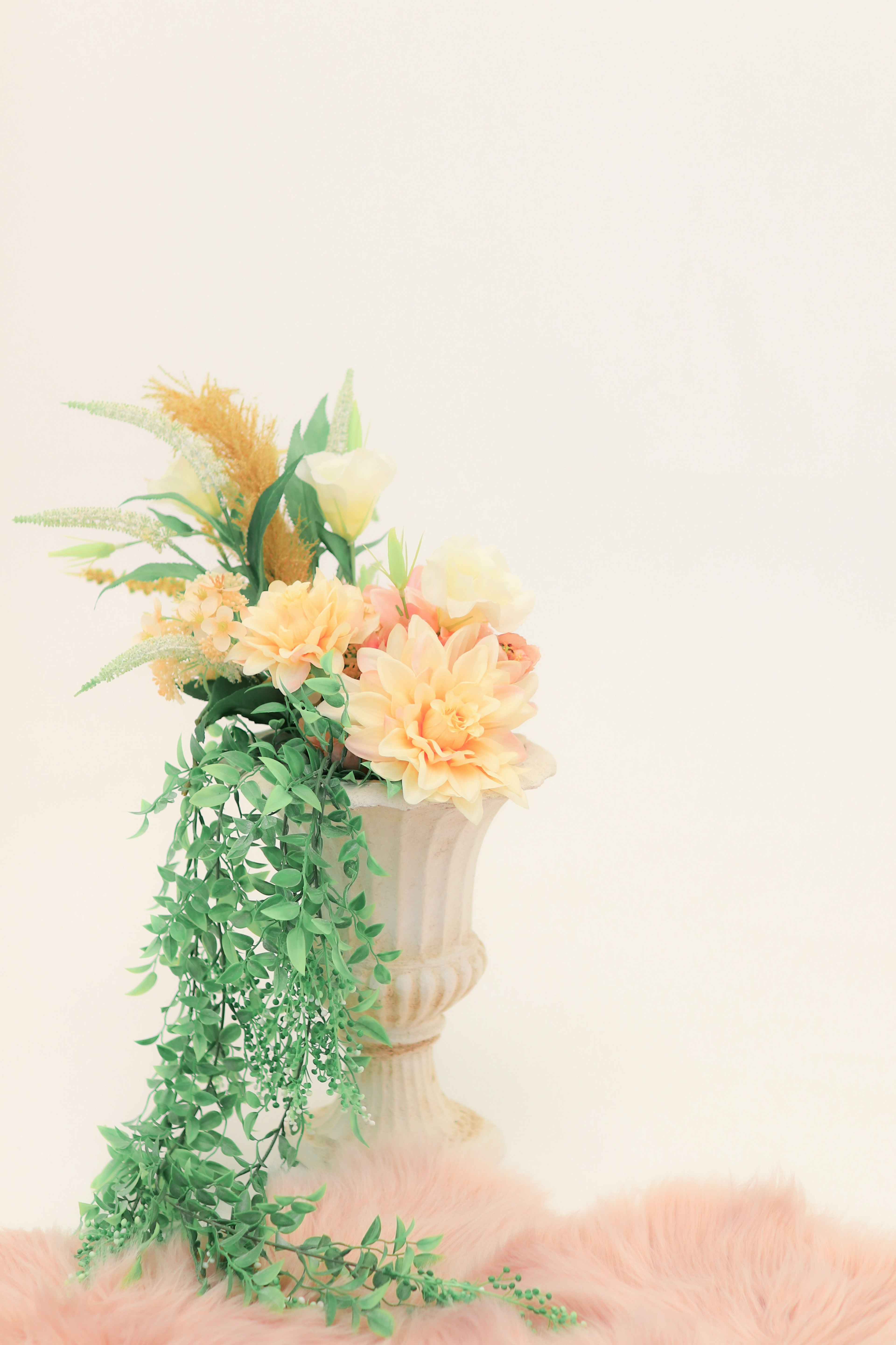 Pale colored flowers arranged in a white vase with green leaves