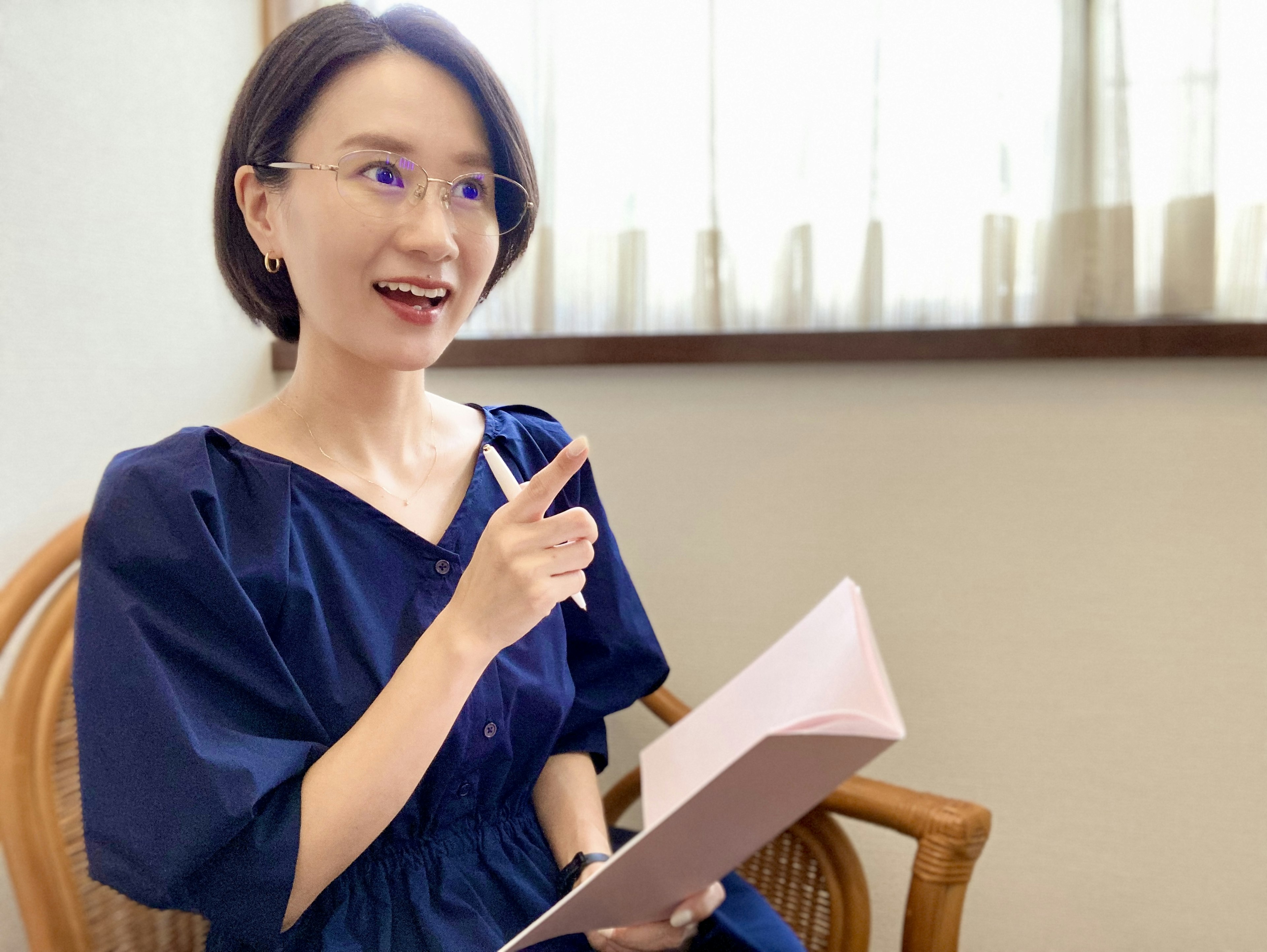 A woman in casual attire holding a notebook and pointing her finger