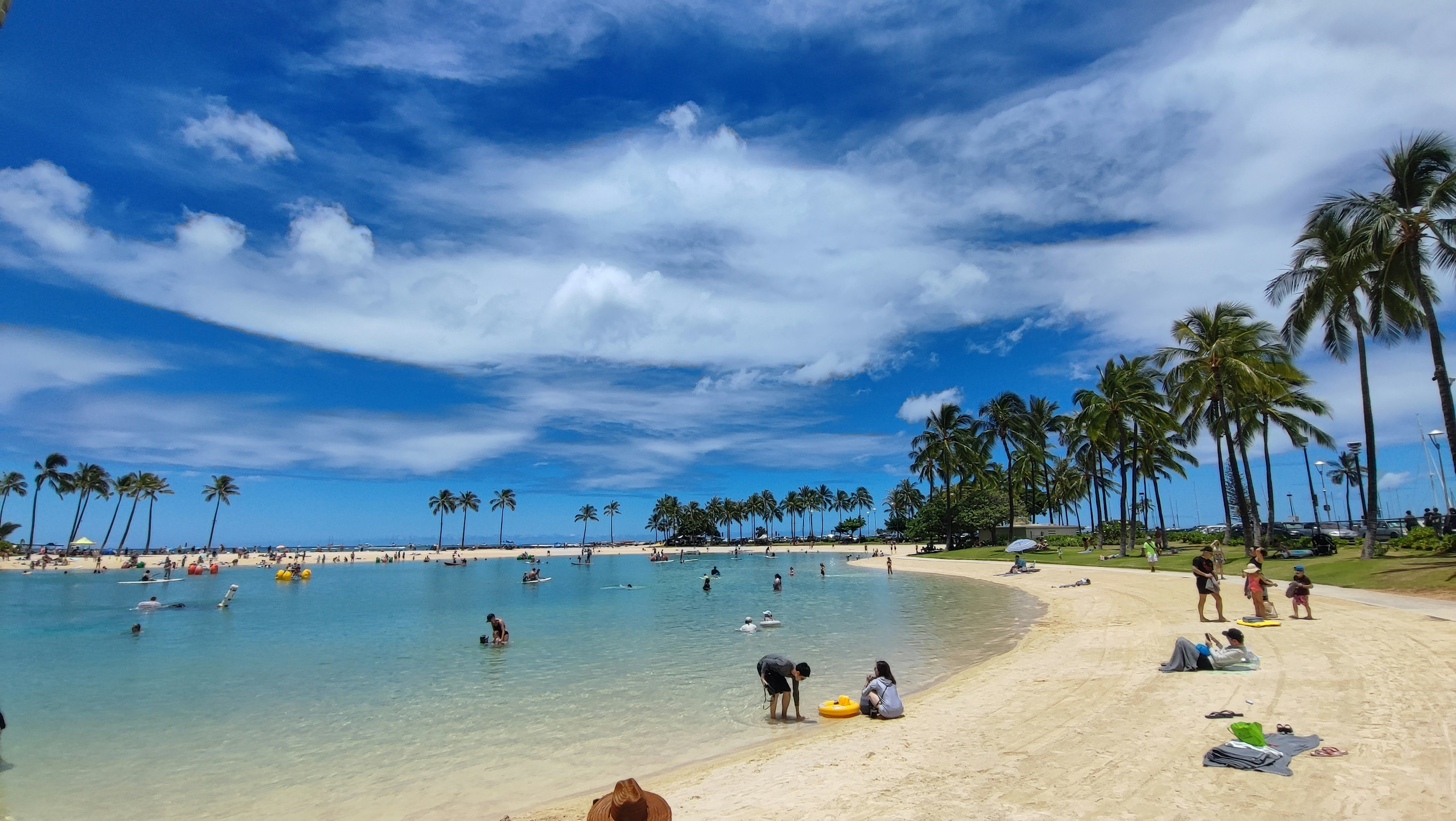 Pemandangan pantai dengan langit biru dan pasir putih di mana orang-orang bersantai