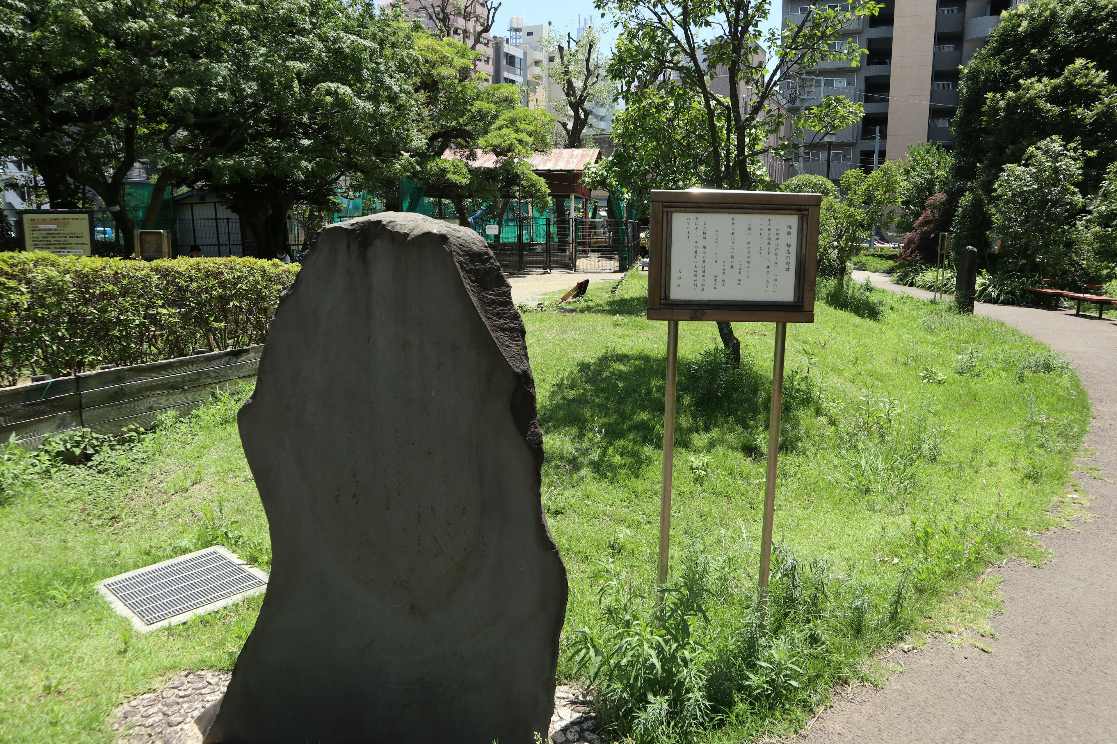 Monumen batu dan papan informasi dikelilingi oleh pepohonan di taman