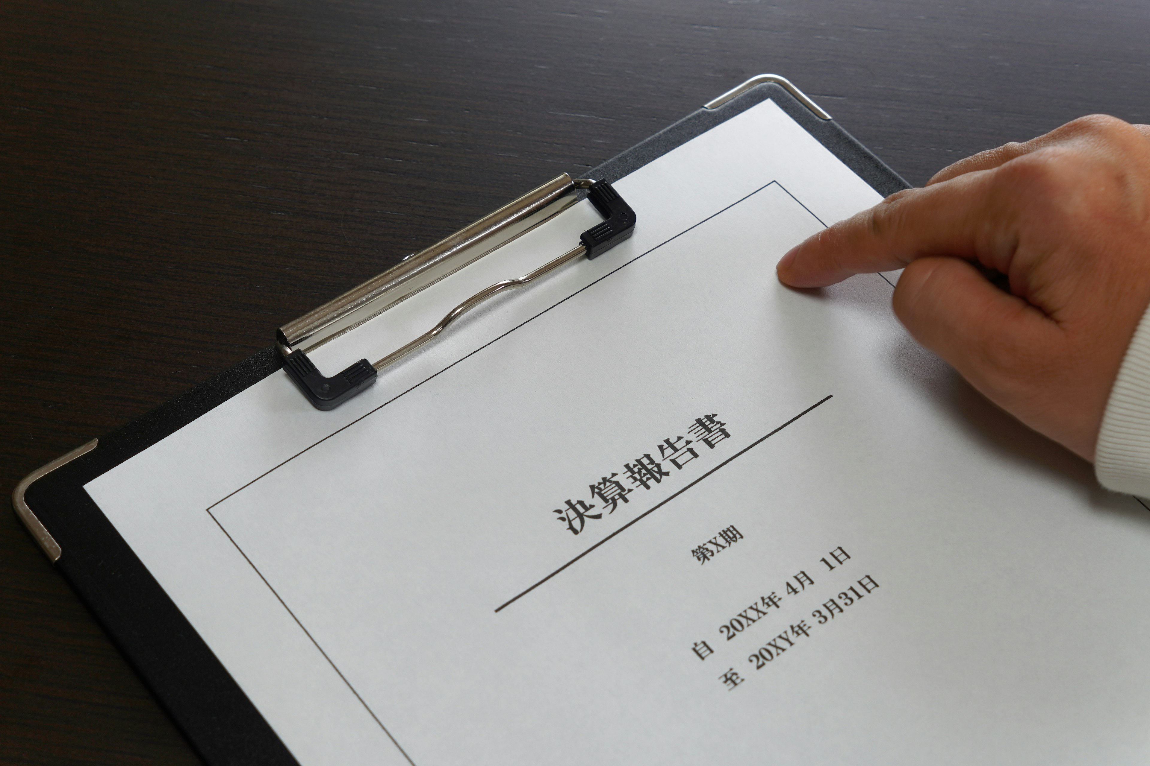 A hand pointing at a document on a clipboard