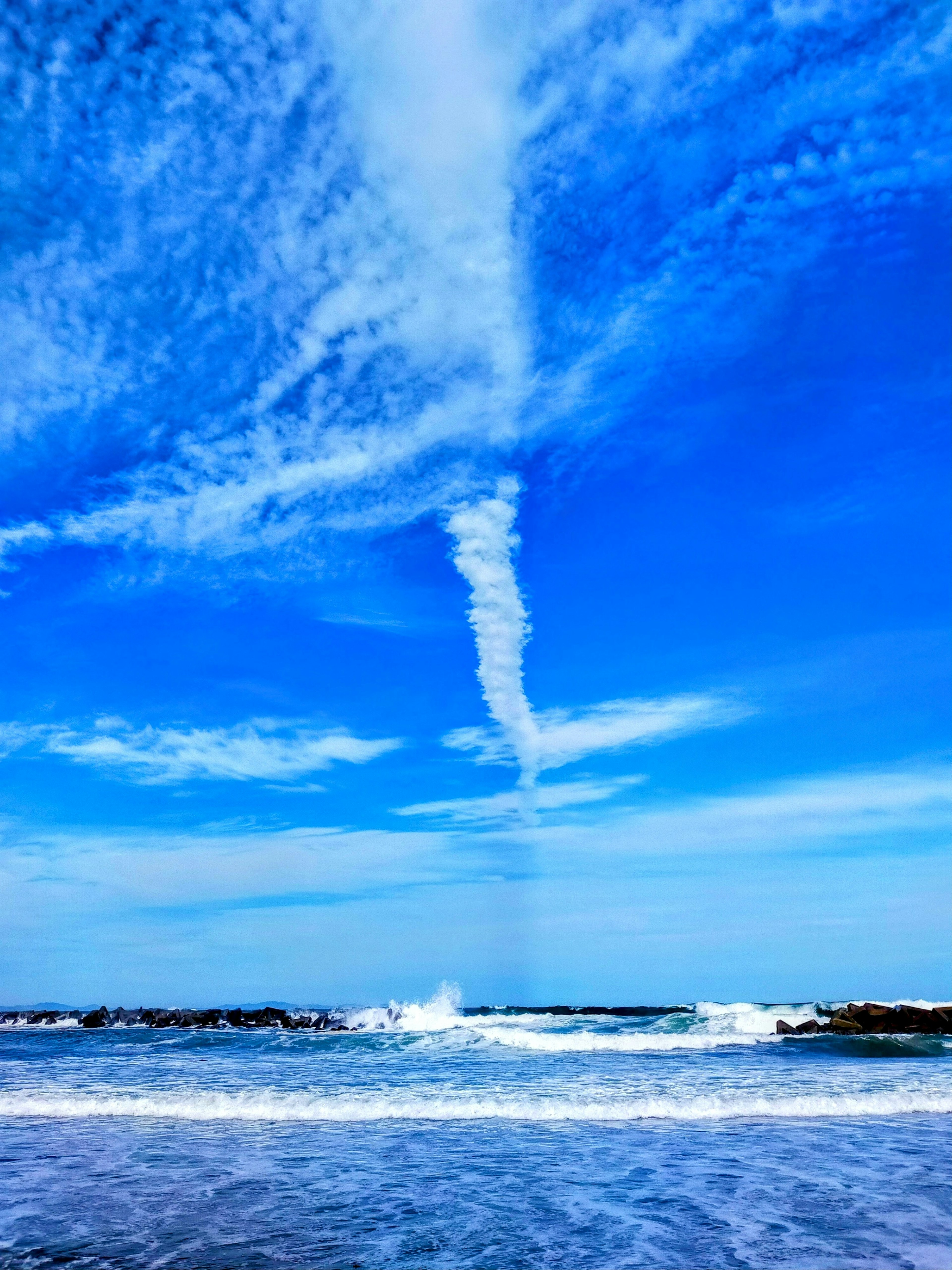 Eine malerische Aussicht auf den Ozean mit Wellen und einer spiralförmigen Wolkenformation im blauen Himmel