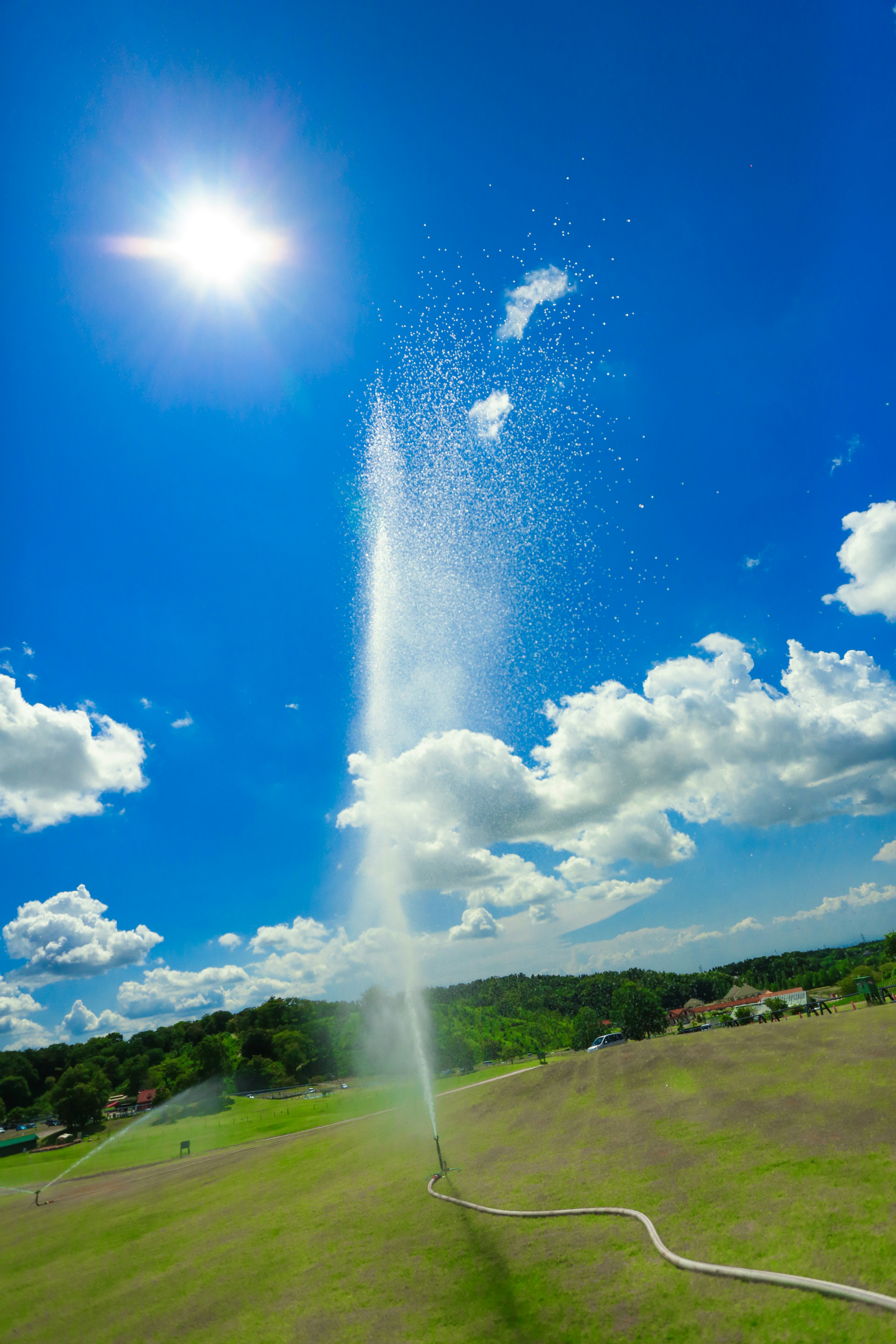 Una fontana che spruzza acqua contro un cielo blu brillante con nuvole e sole