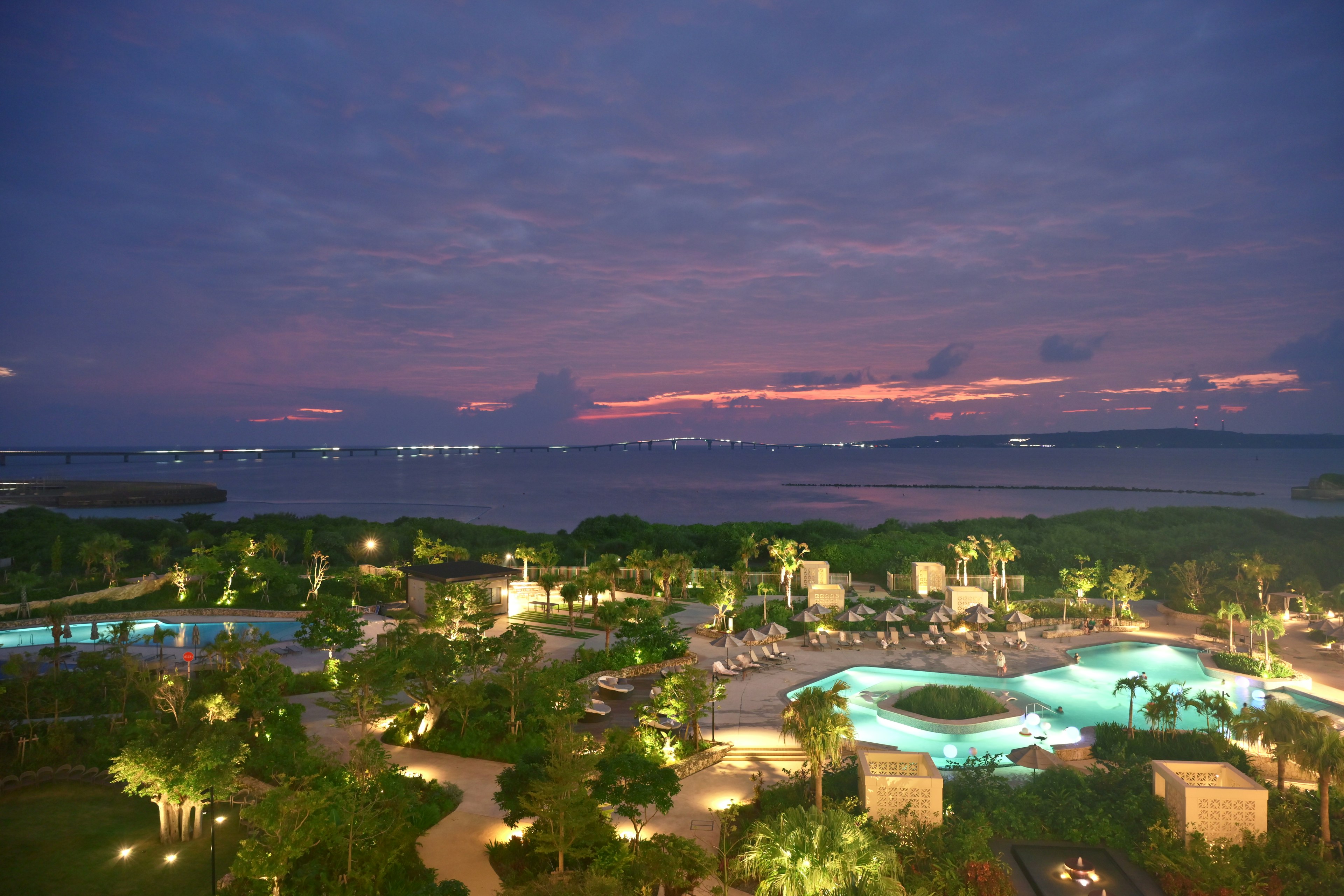 Dämmerungsansicht eines Resorts mit Pools und üppigen Gärten mit Blick auf das Meer