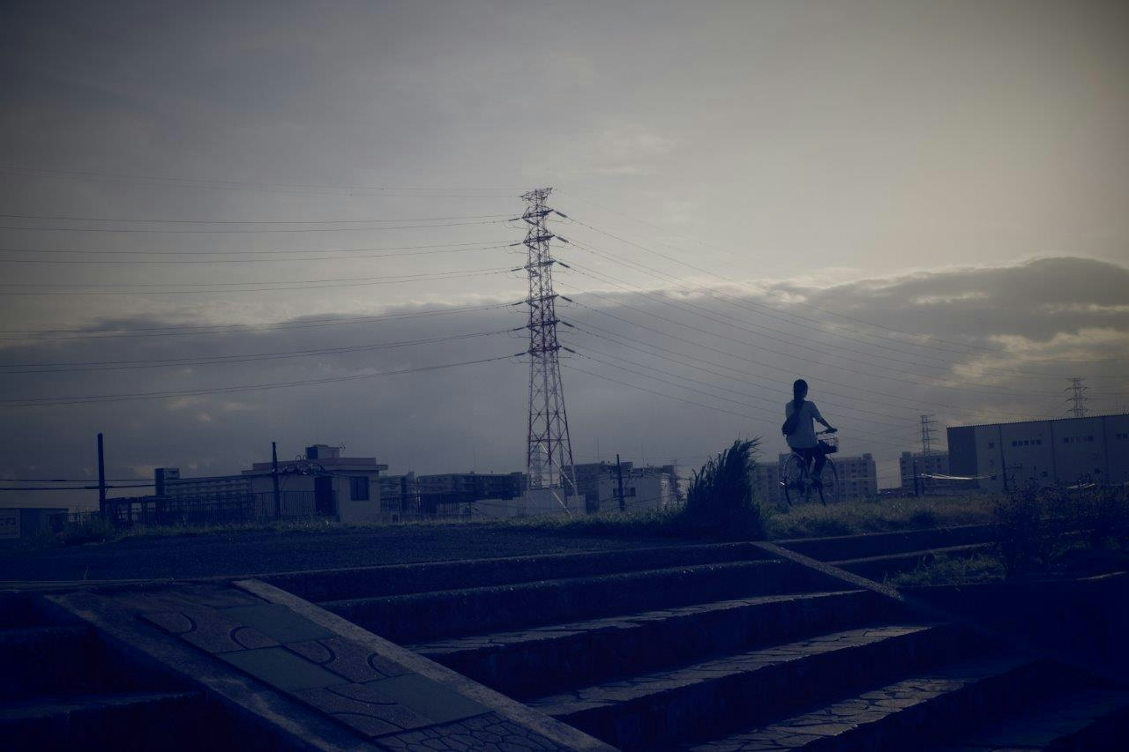 Silueta de una persona montando en bicicleta bajo un cielo tenue con líneas eléctricas