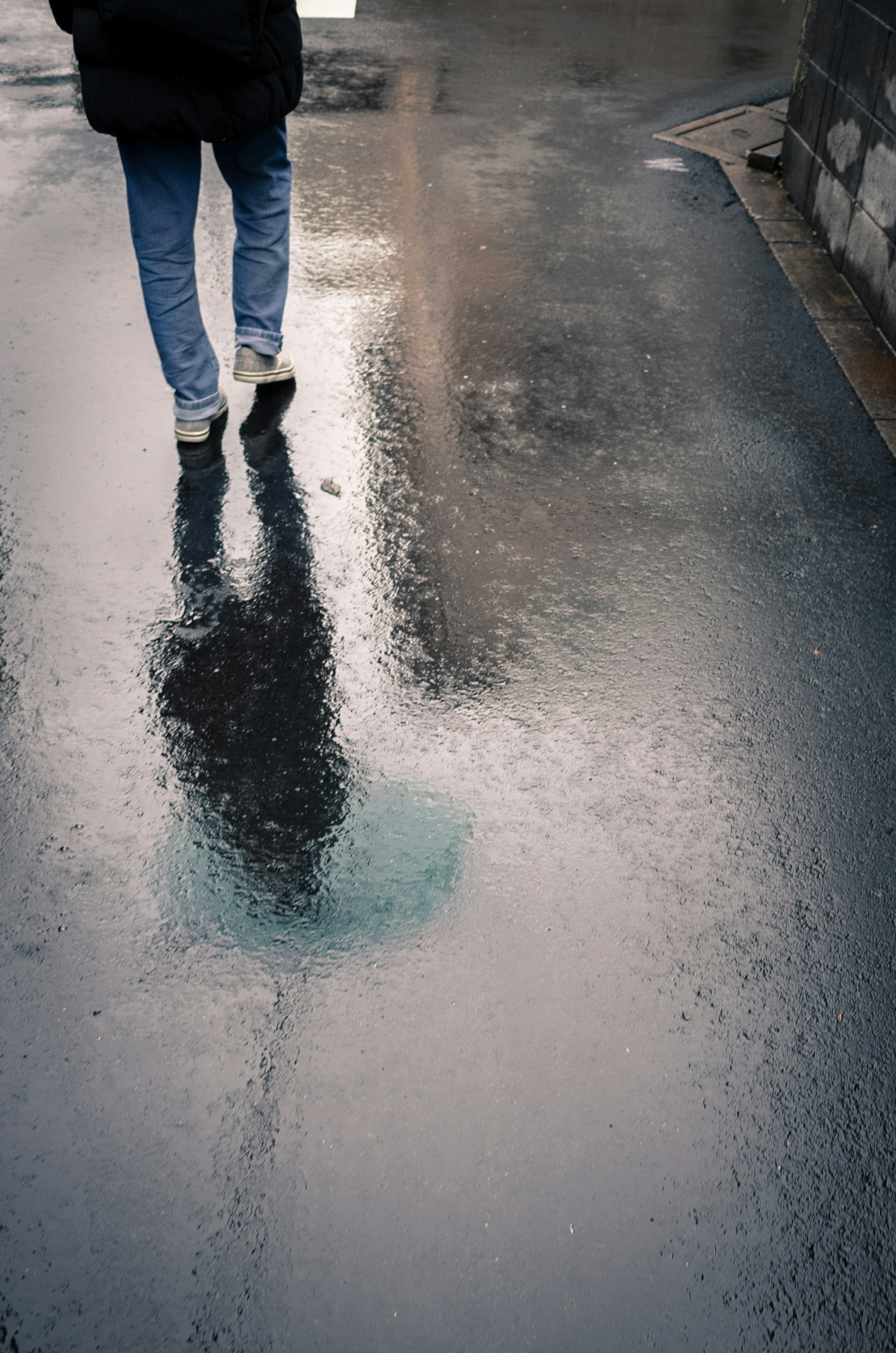 Une personne marchant sur un trottoir mouillé avec un reflet dans une flaque d'eau