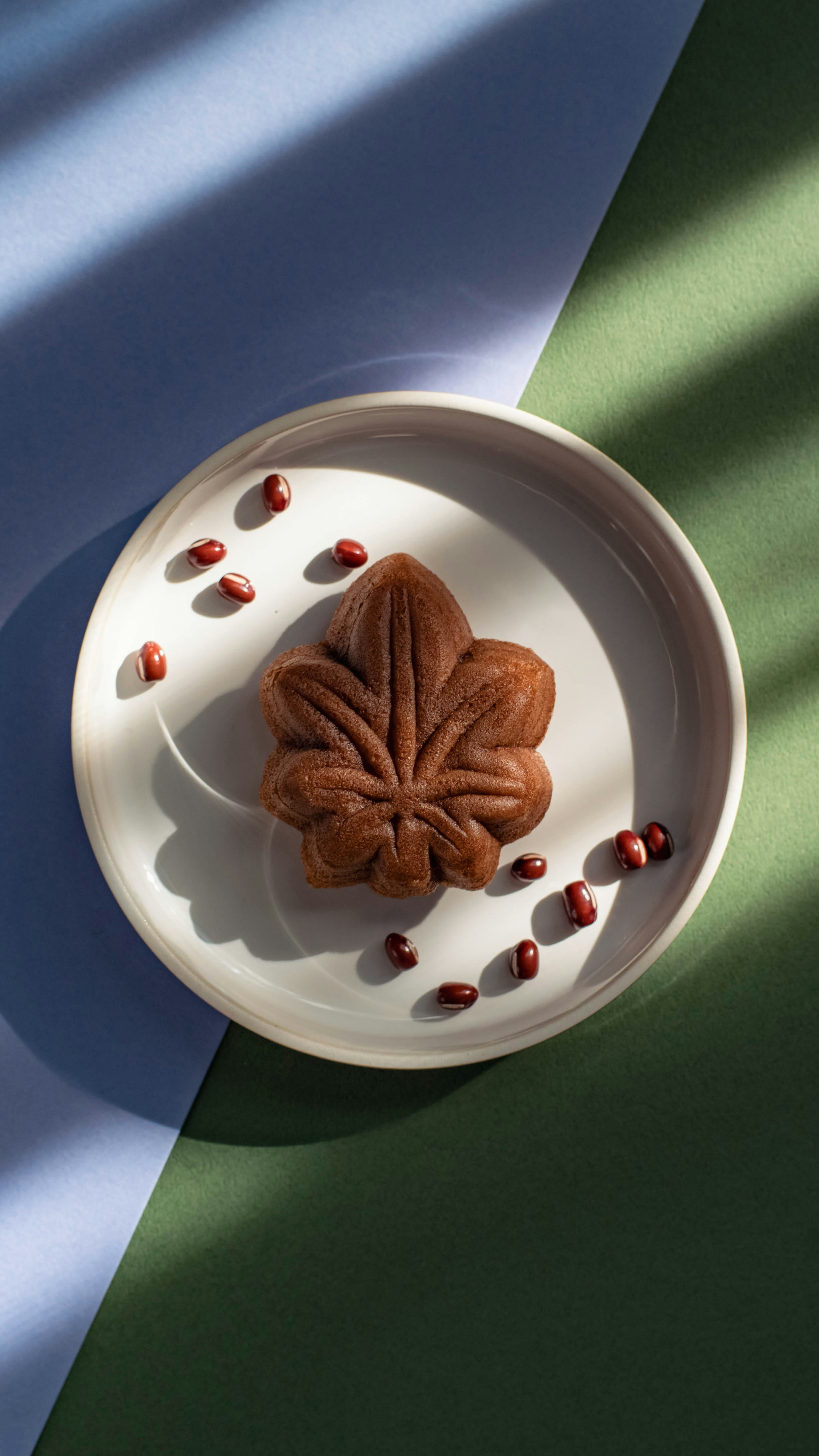 A leaf-shaped pastry on a white plate surrounded by scattered red beans