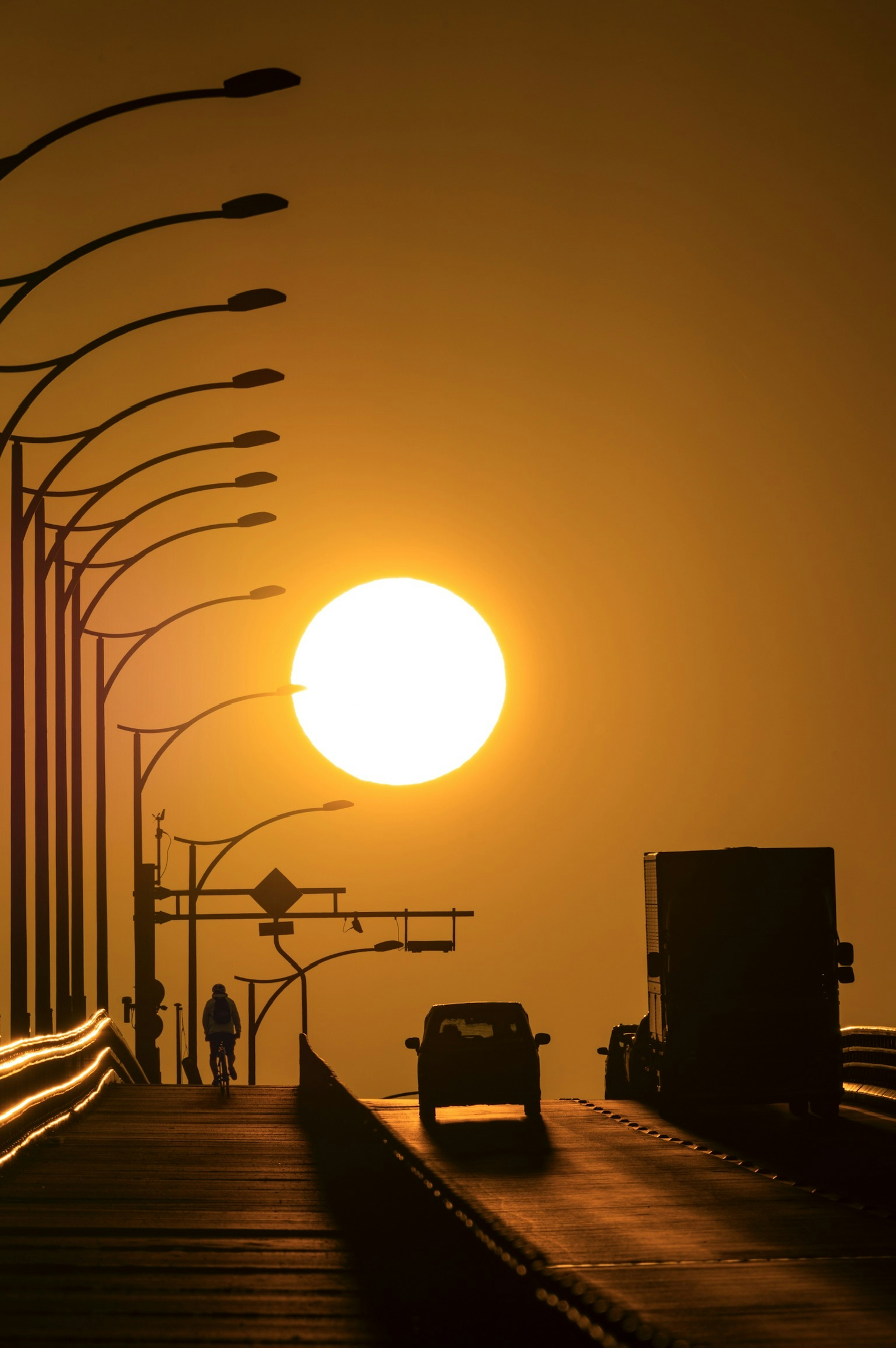 Silhouette matahari terbenam di jembatan dengan mobil dan orang yang melintas