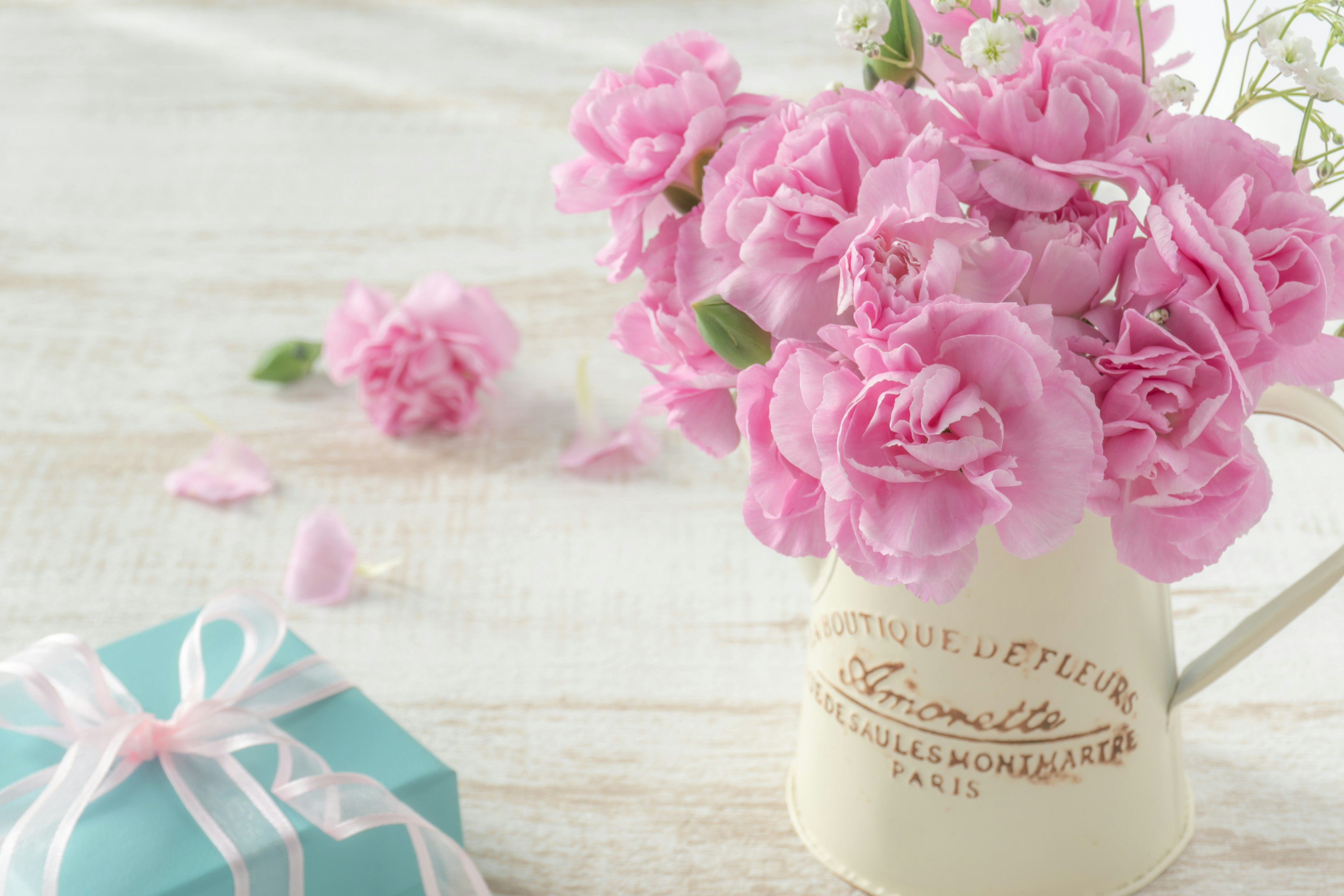 Pink carnations in a white vase with a blue gift box