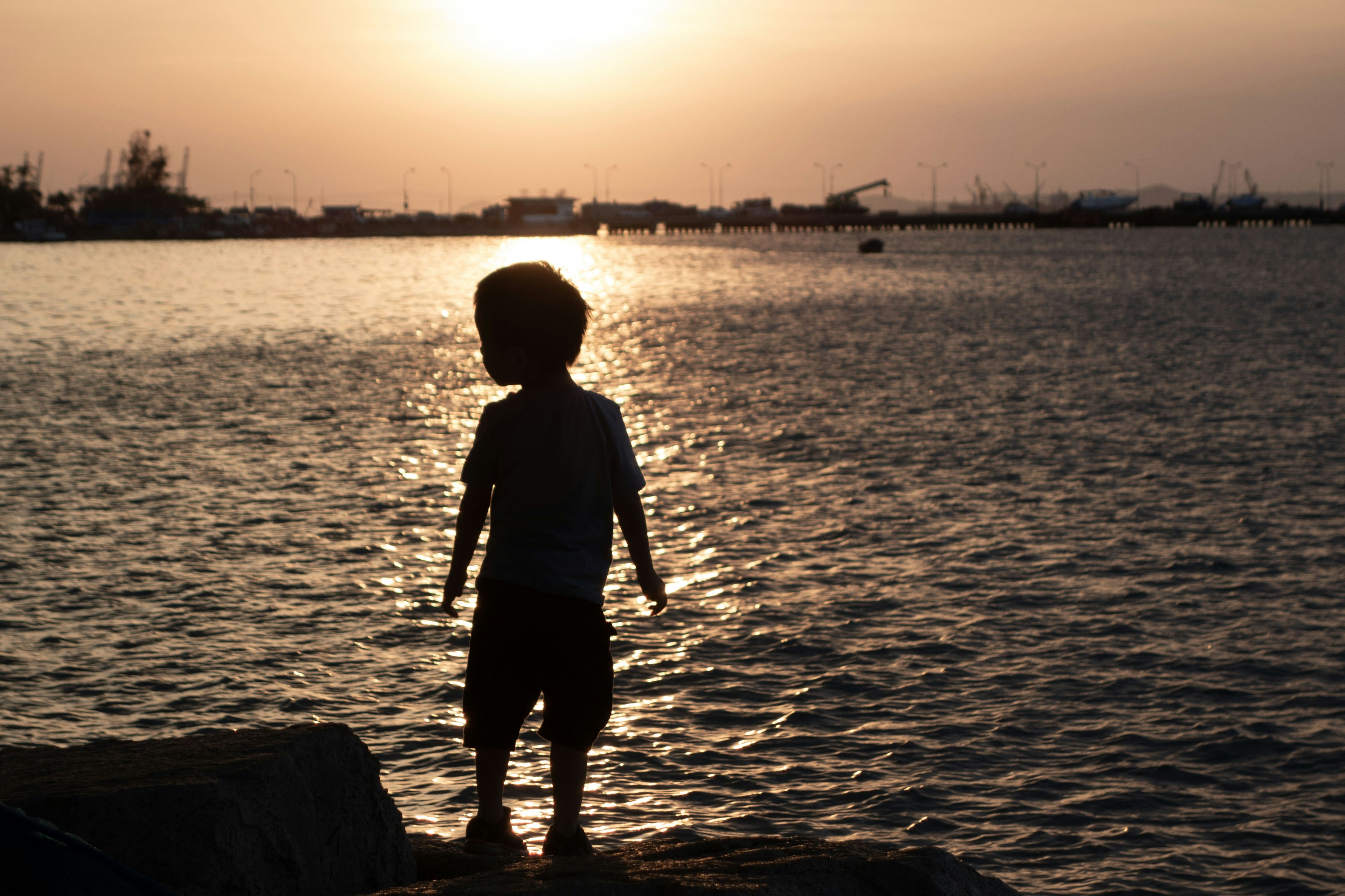 夕陽下站在海邊的孩子剪影