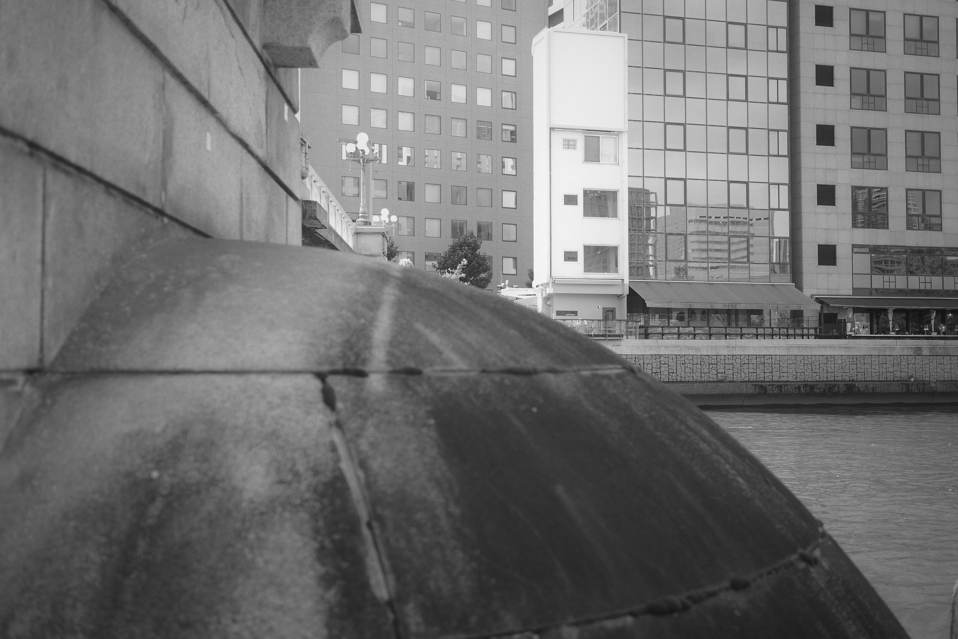 Foto en blanco y negro con un ángulo cercano del borde curvo de un puente y edificios cercanos