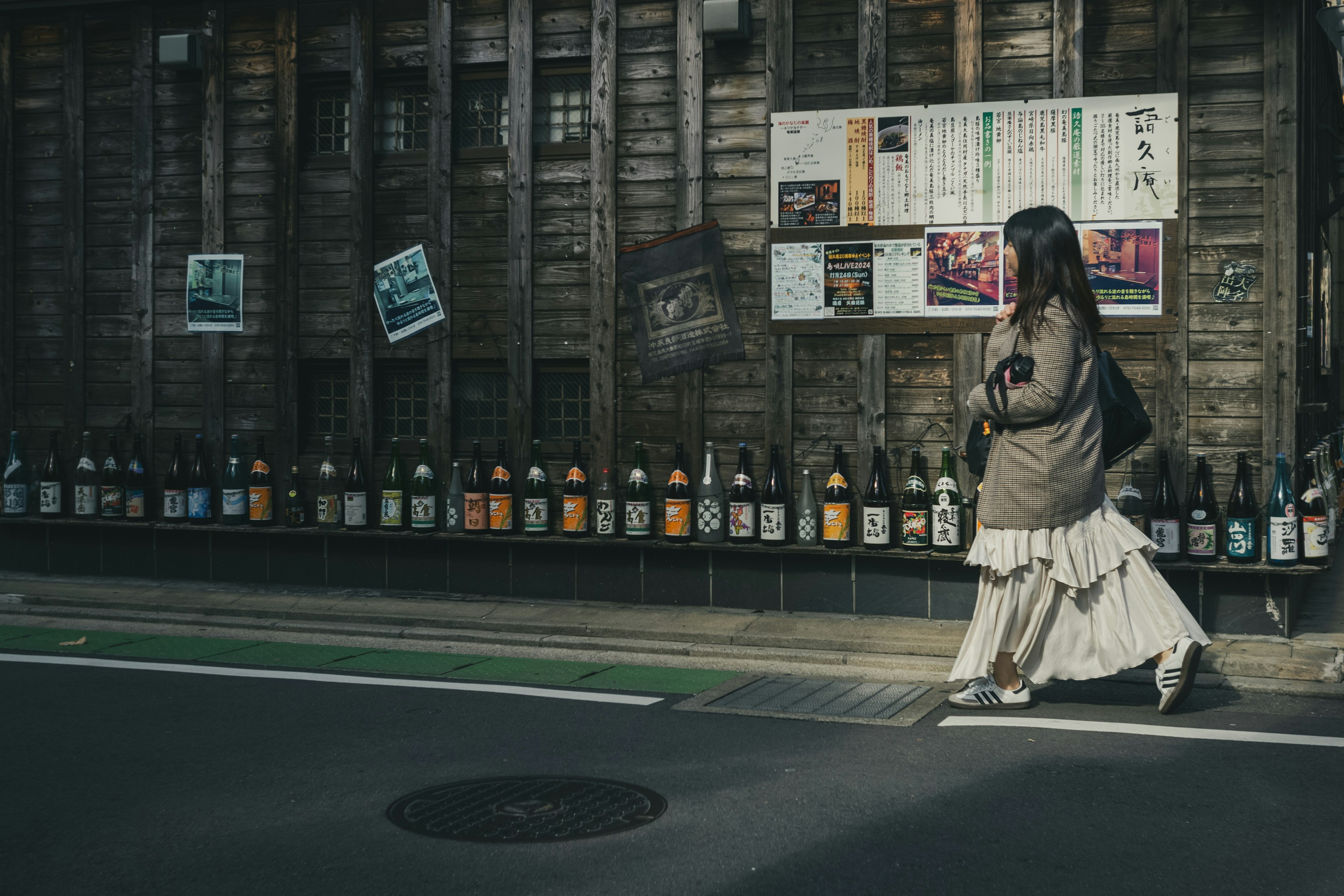 一名女性在日本街角走過，旁邊排列著清酒瓶