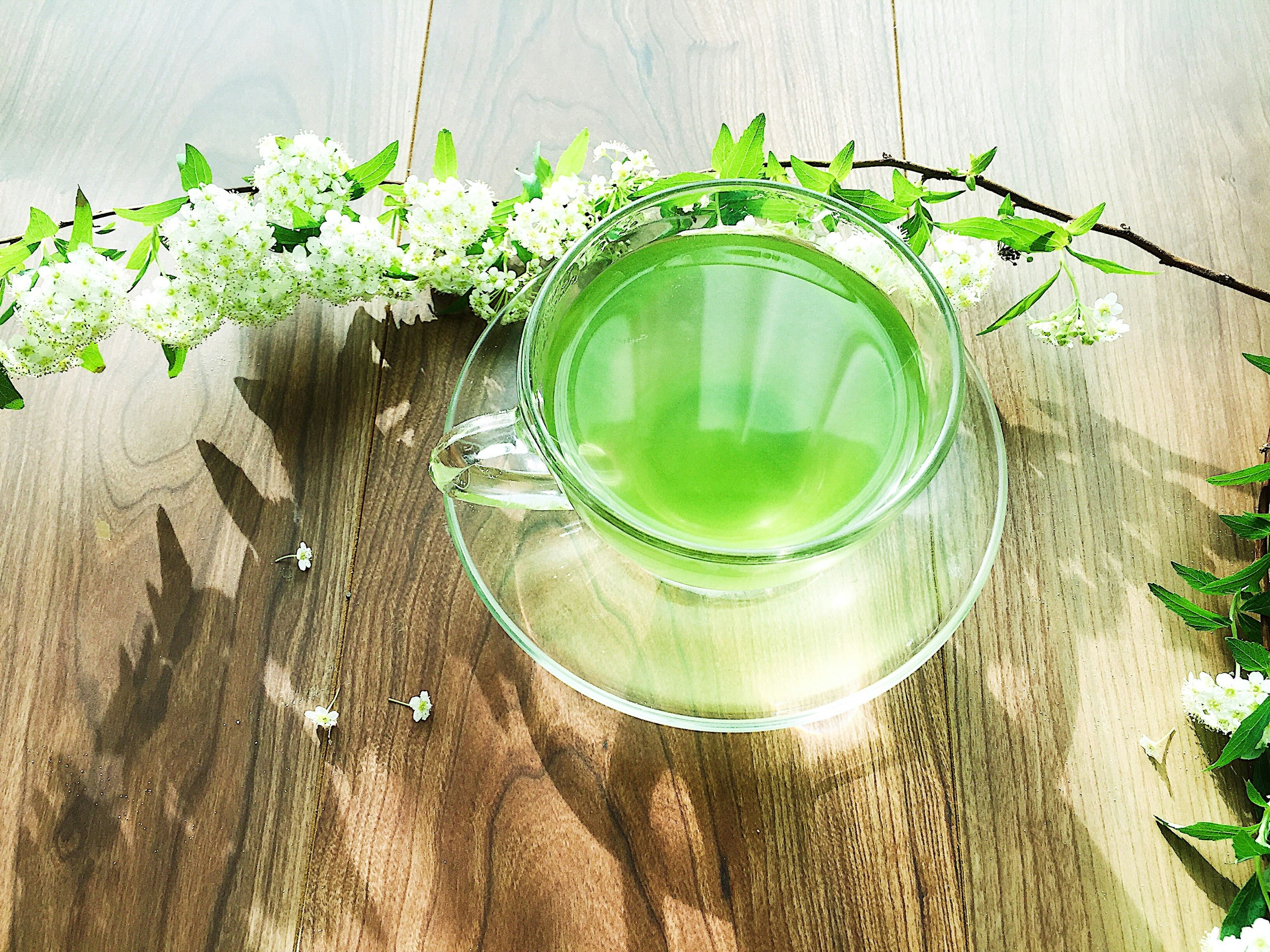 Tasse en verre de thé vert entourée de fleurs blanches