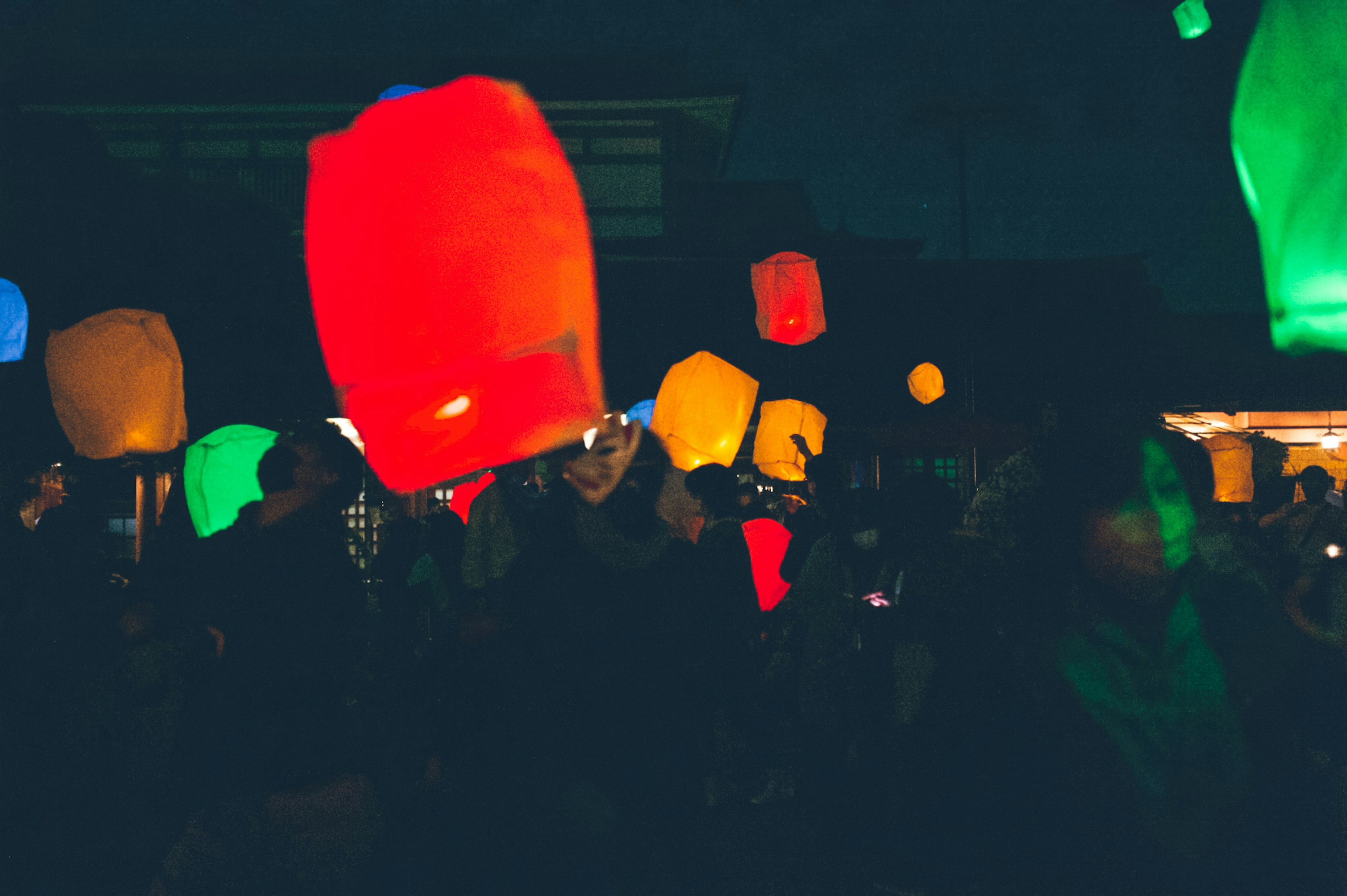 Des lanternes colorées flottant dans le ciel nocturne avec des silhouettes de personnes