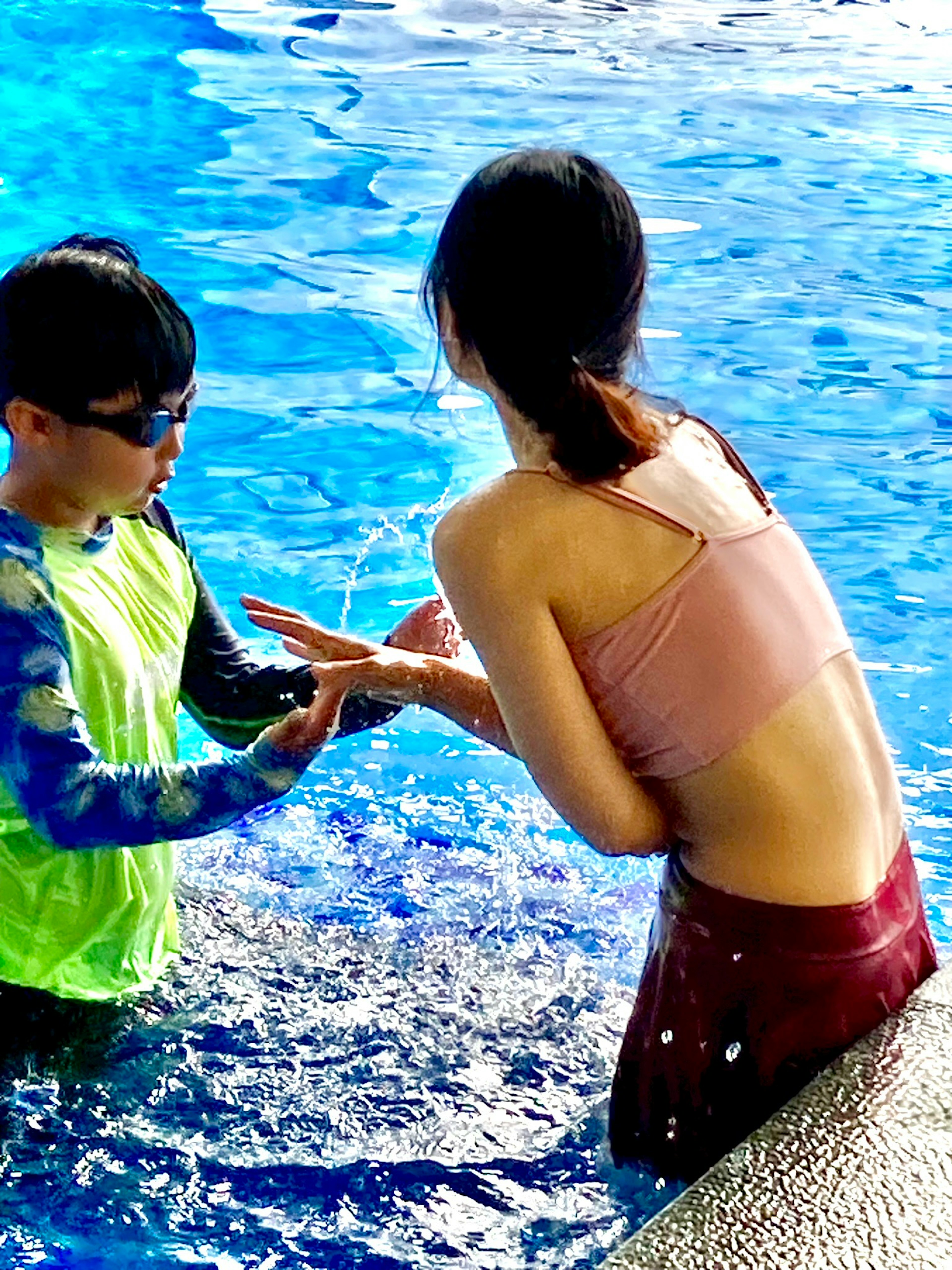 Seorang anak dan wanita berinteraksi di kolam renang dengan percikan air