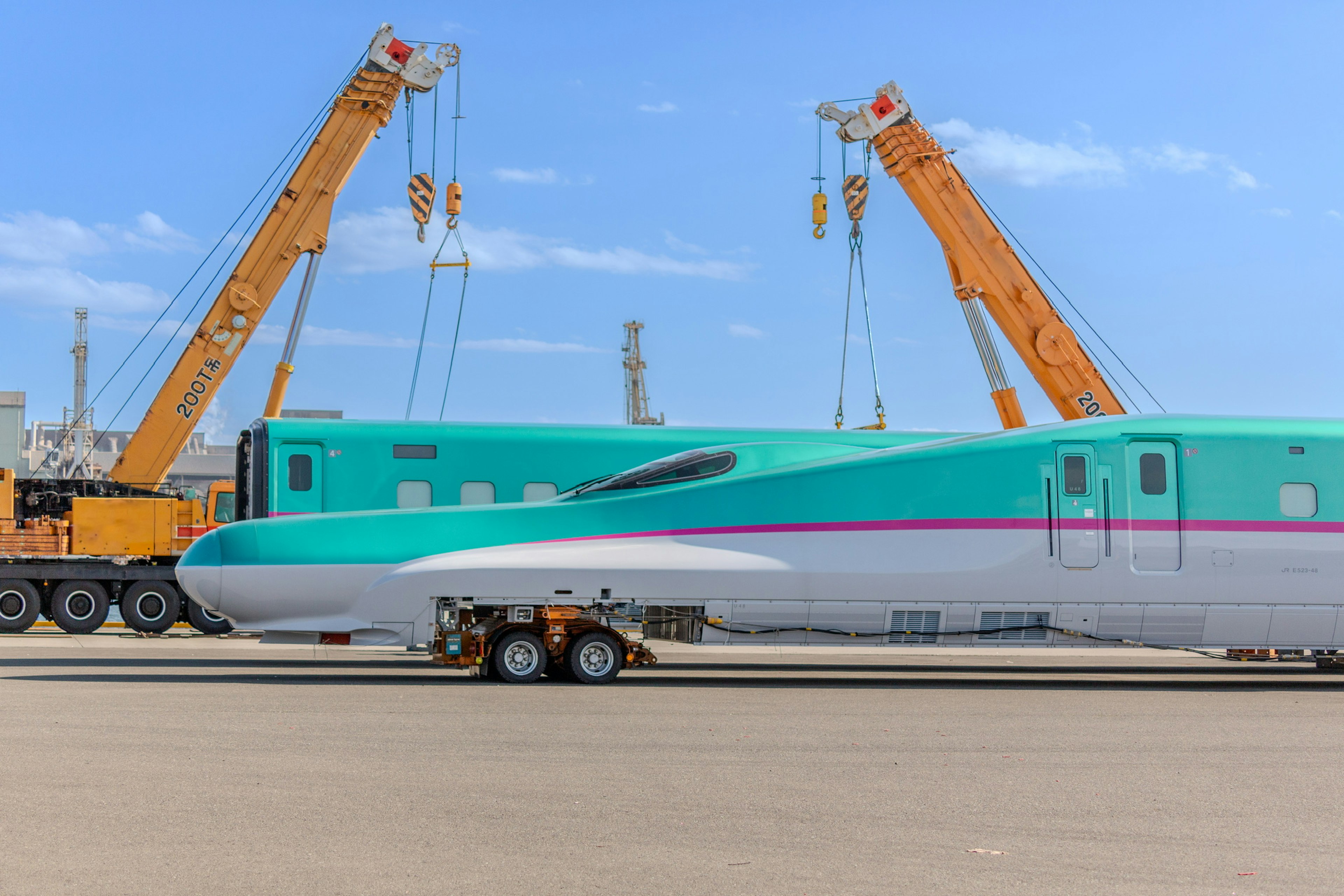 A turquoise airplane being lifted by cranes at an airport