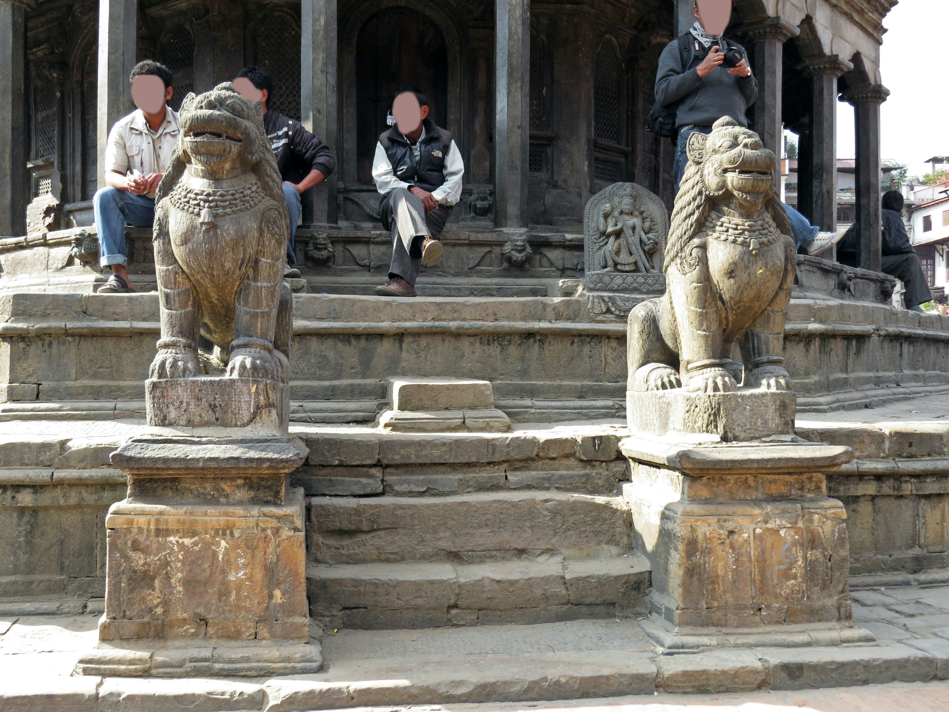 People sitting on the steps of a temple with sculpted lion statues